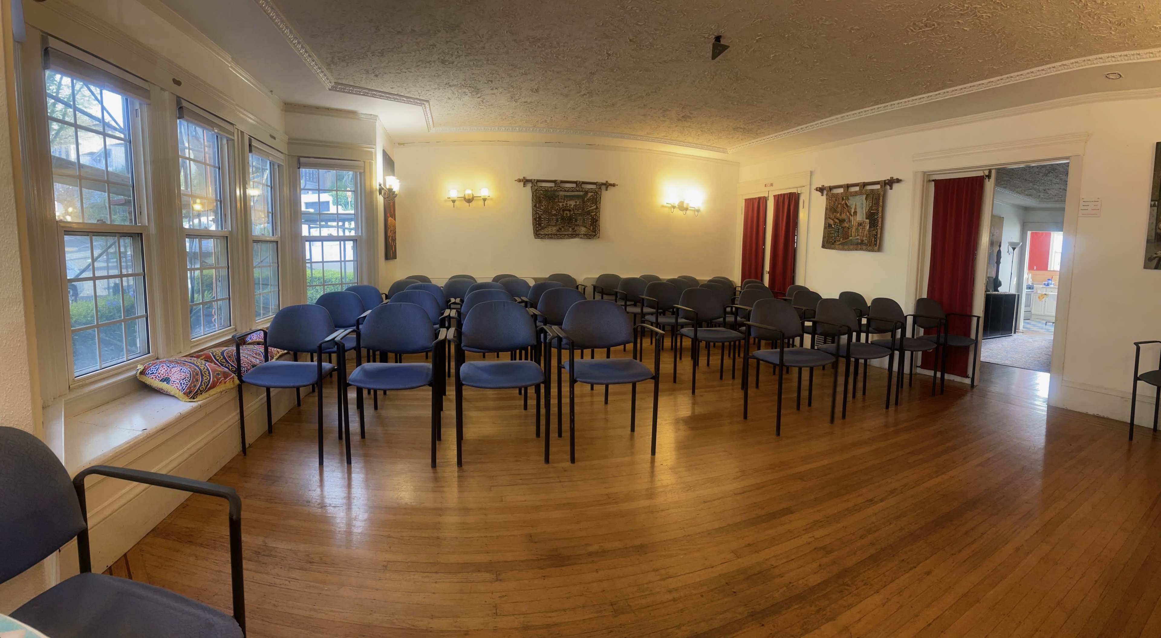A room with wooden floors contains rows of blue chairs and paintings on the walls.