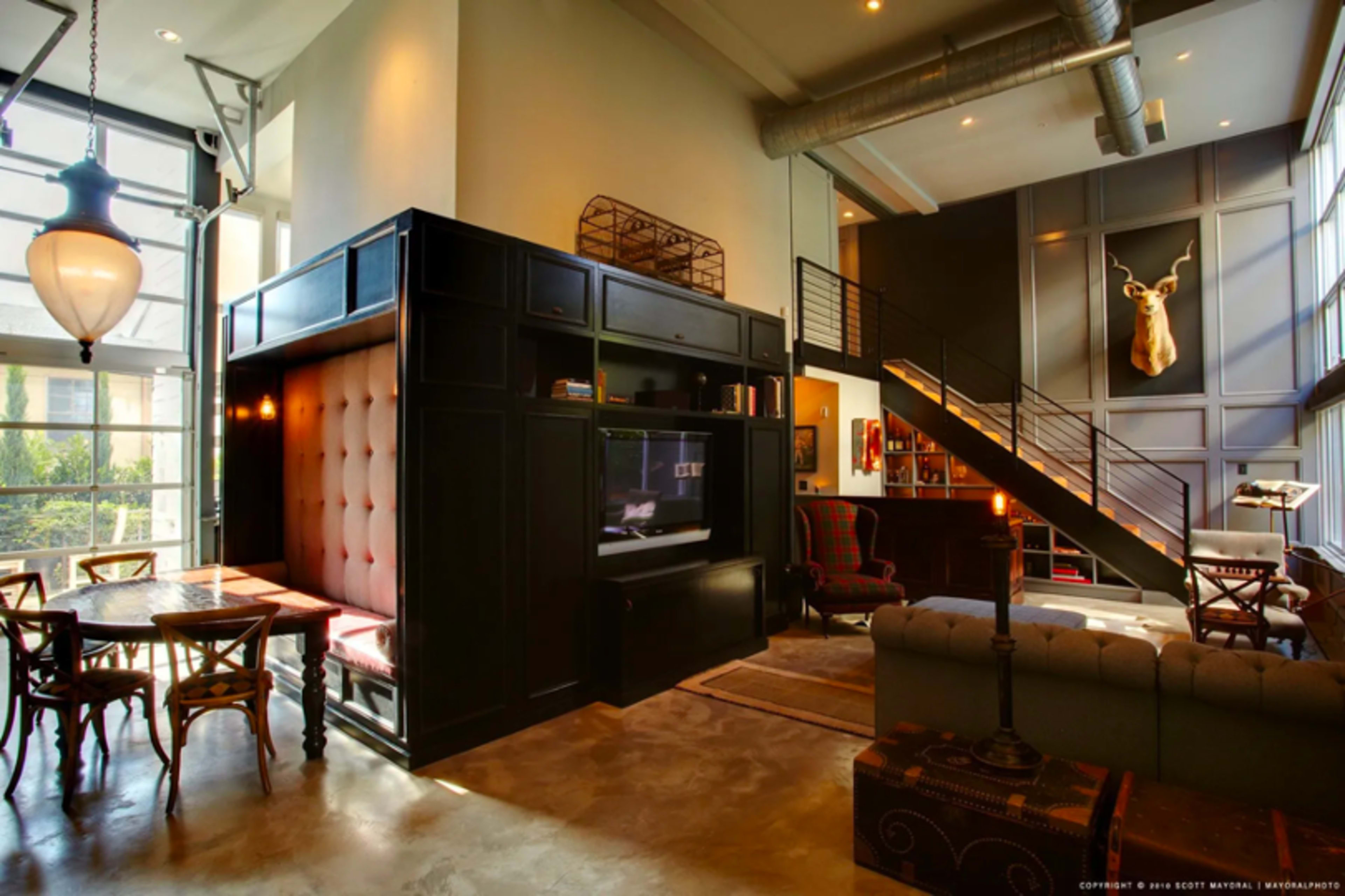 A modern living space with a mix of seating areas, a staircase, and a decorative wall mounted with a deer head.