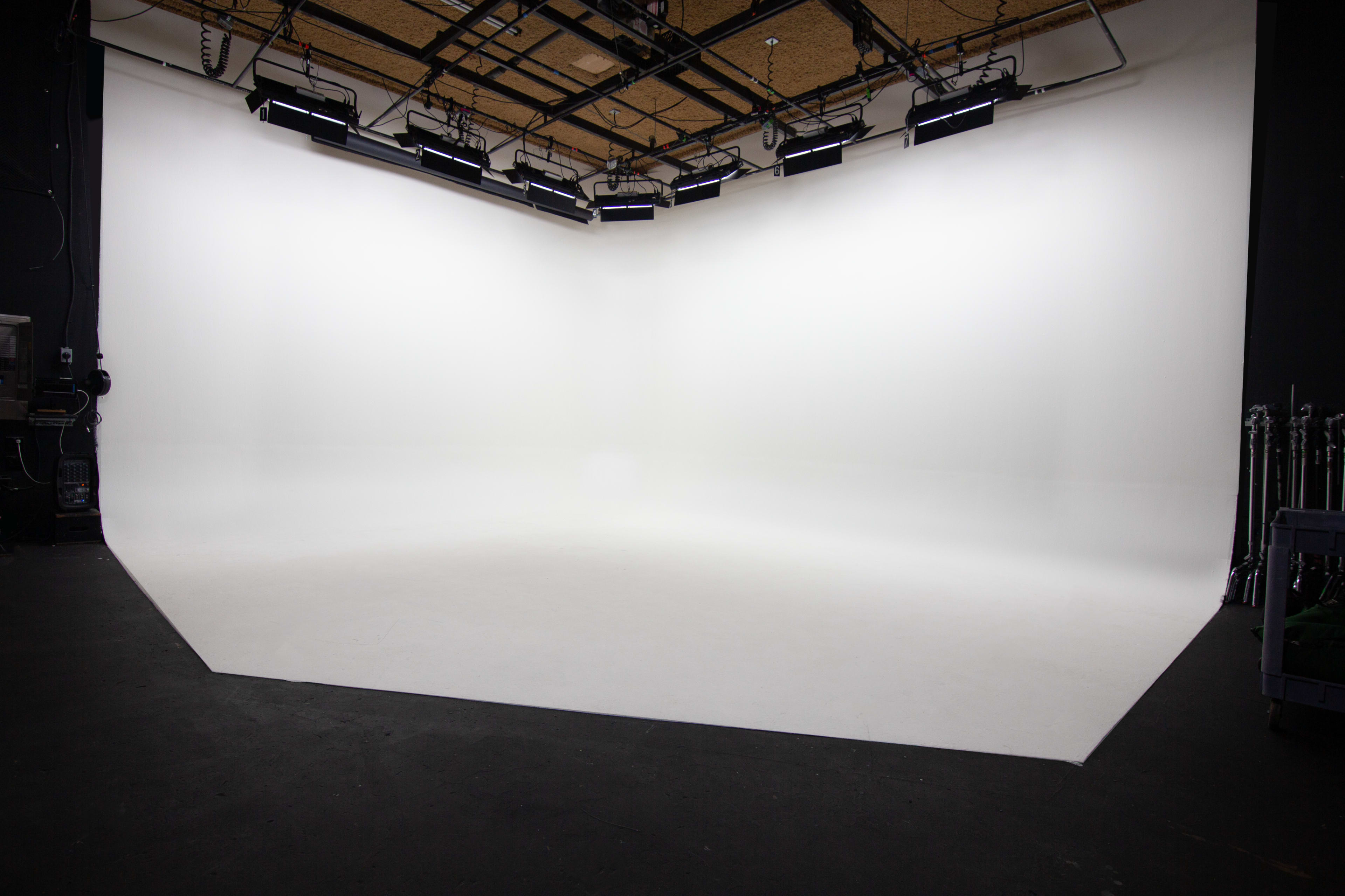 An empty photo studio with a seamless white backdrop and overhead lighting.