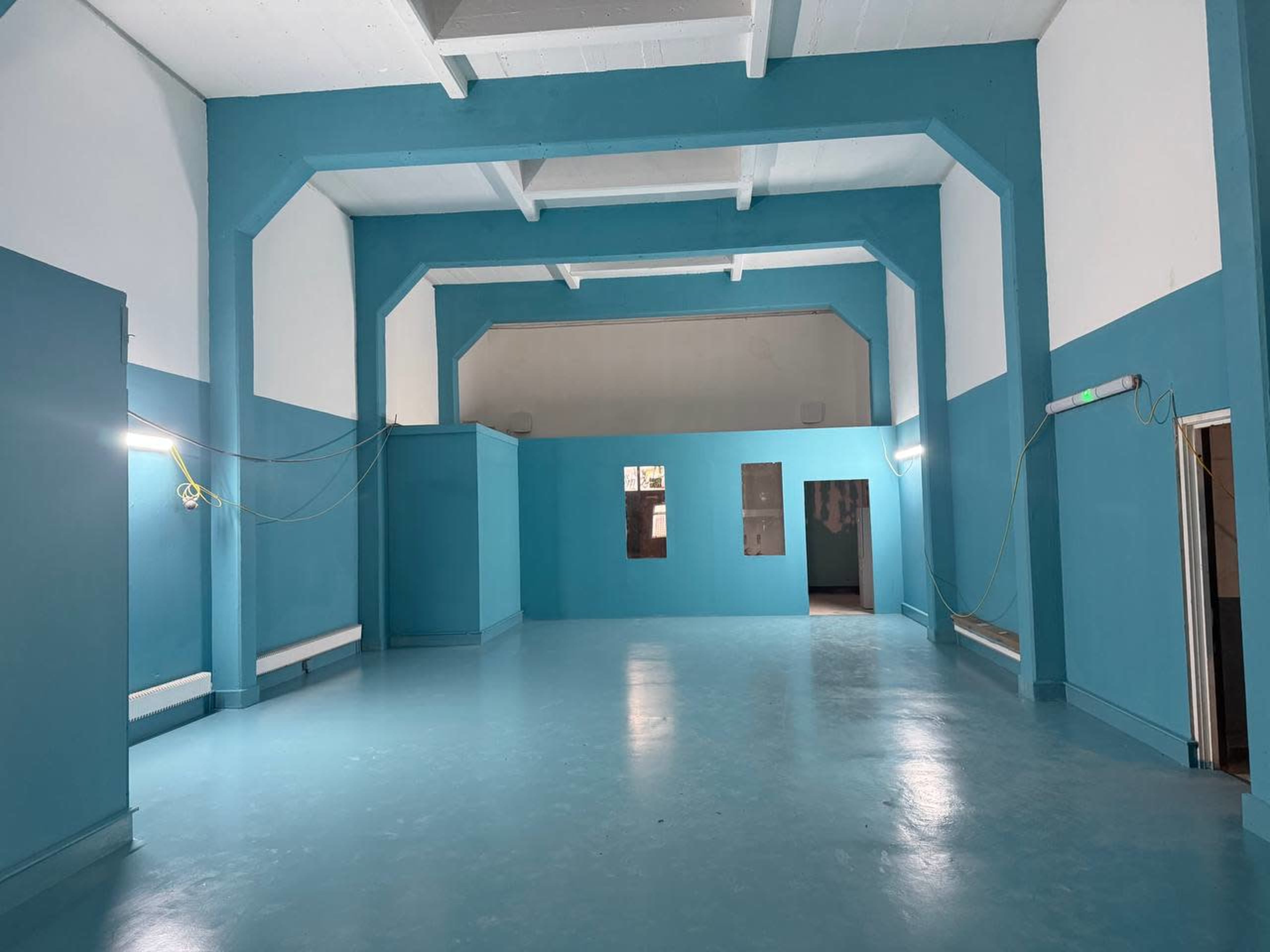 The image shows a spacious interior with blue walls, a polished floor, and minimal lighting.