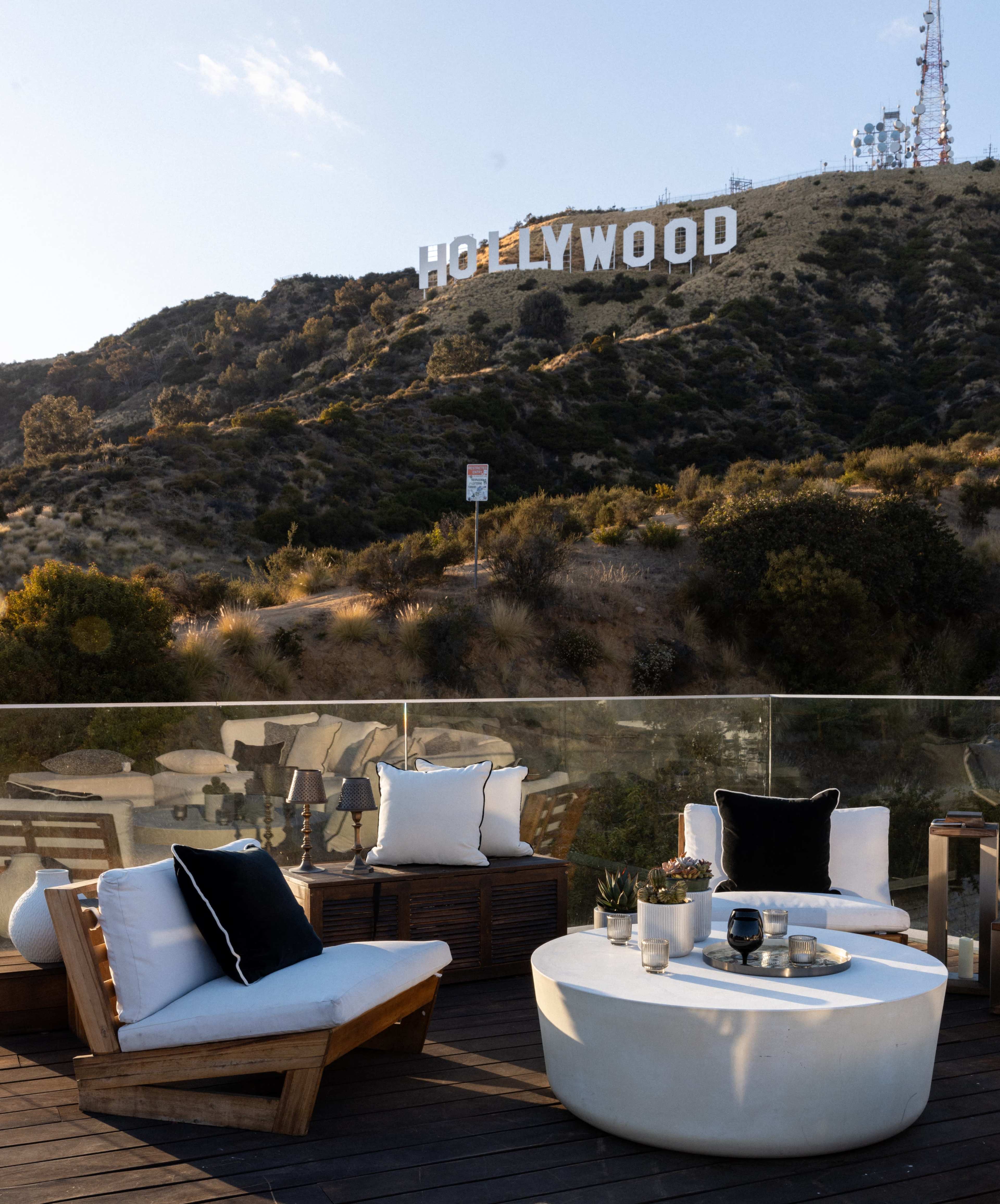 A modern outdoor seating area with plush cushions overlooks the Hollywood sign on a hillside.