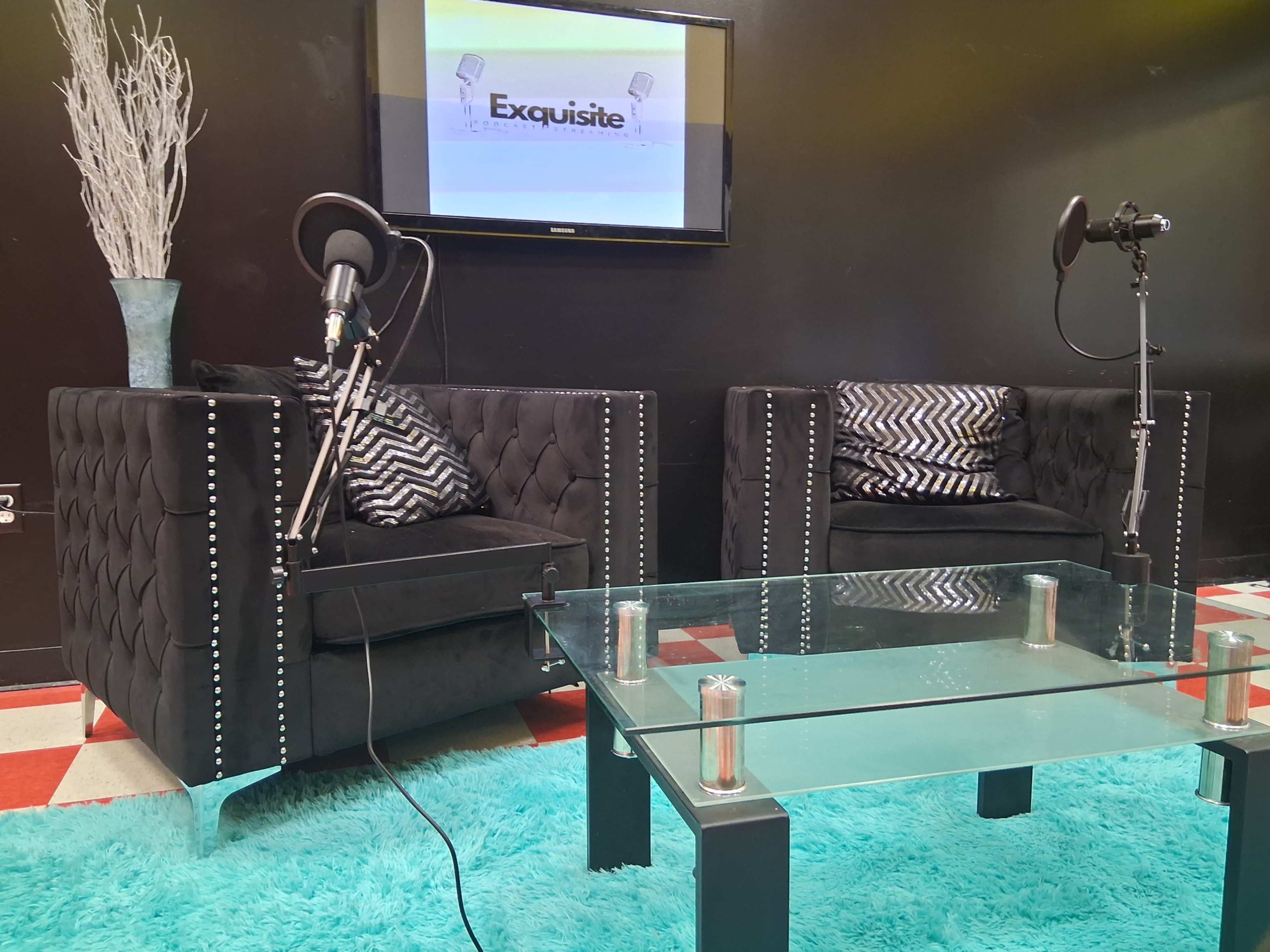 The image features a modern interview setup with two black tufted sofas, a glass coffee table, and a television displaying the word "Exquisite," accompanied by microphones on stands.