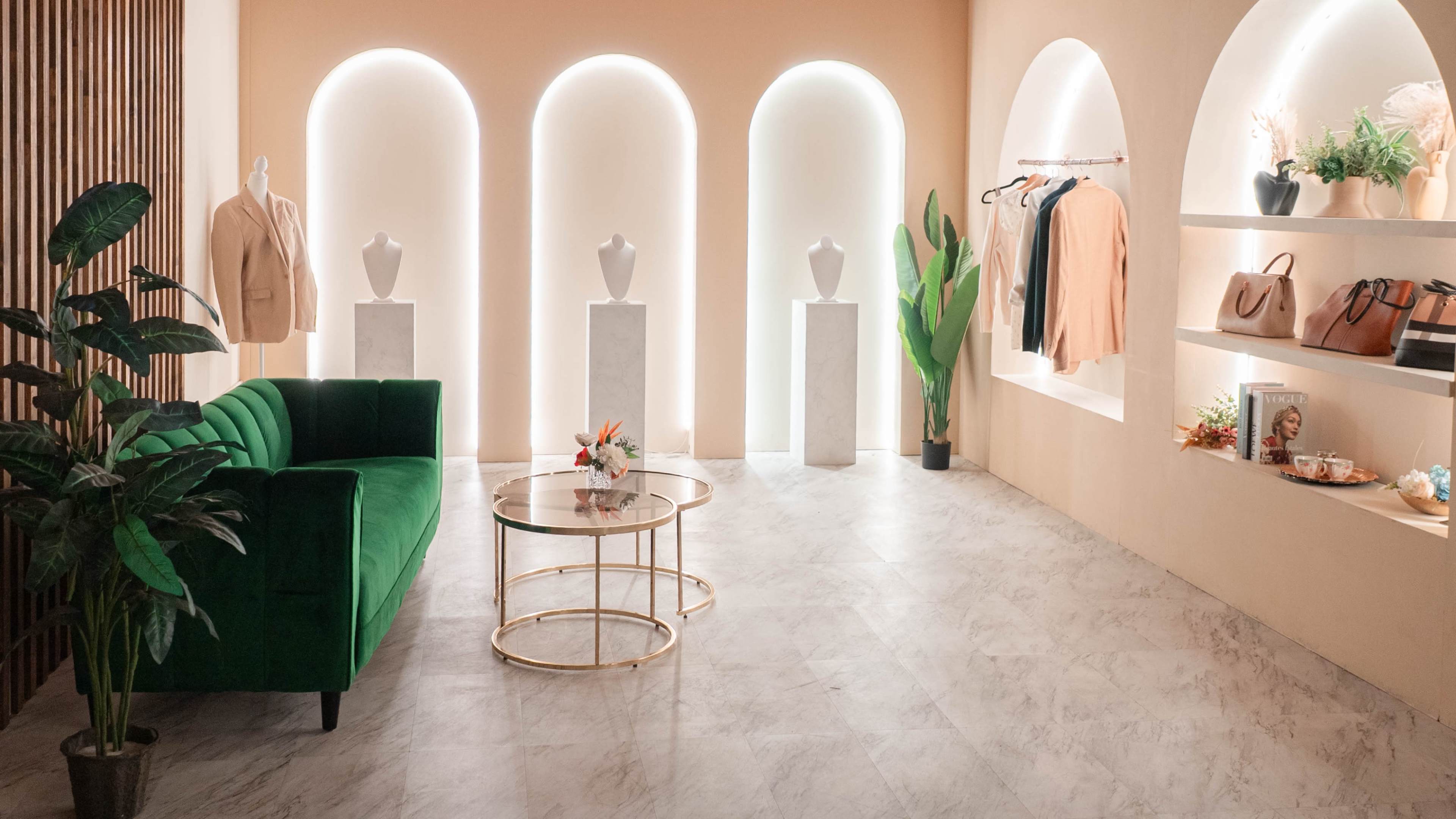 The scene features a stylish boutique interior with arches, a green velvet sofa, marble displays holding clothing, and decorative plants.