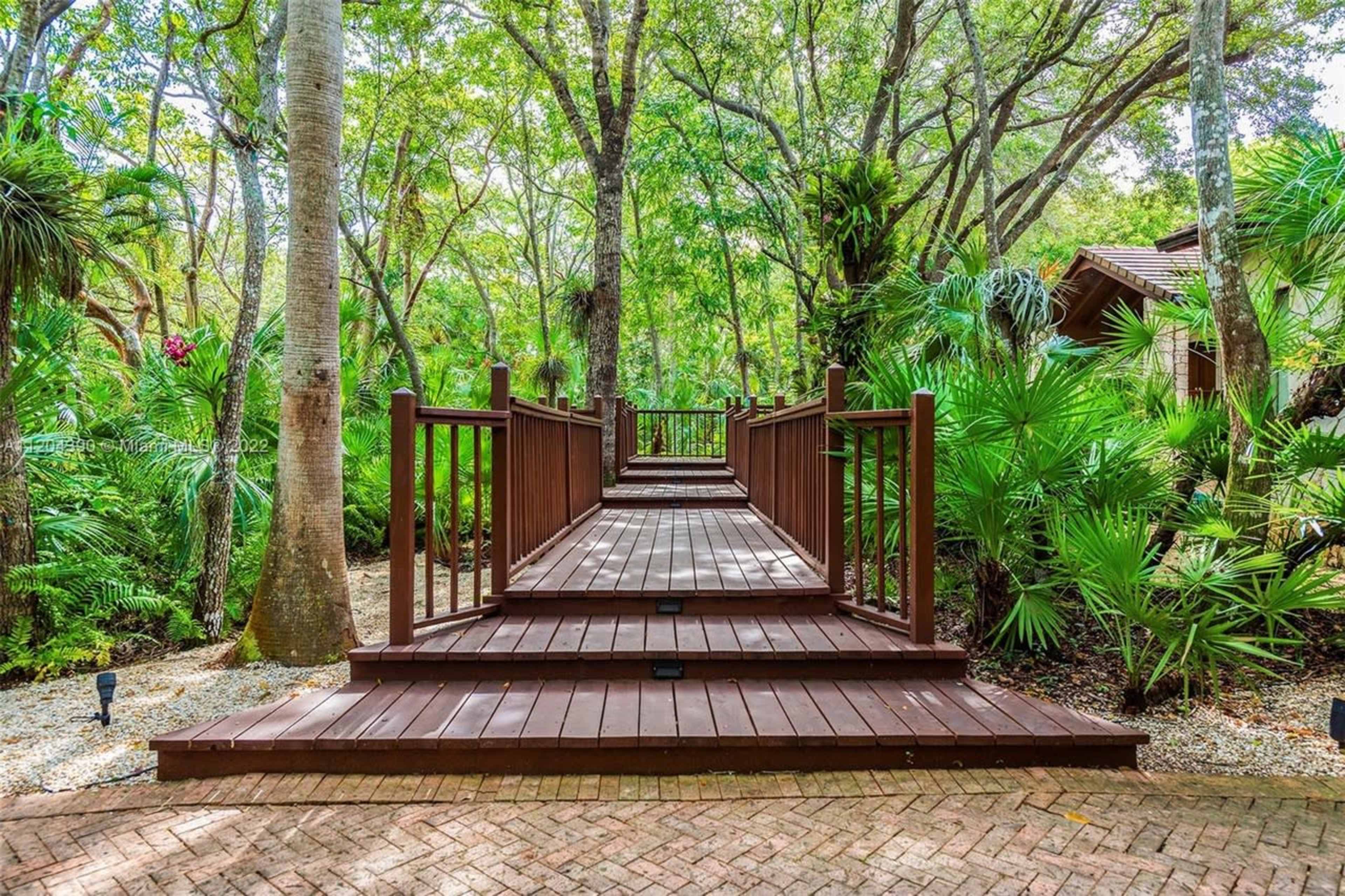A wooden walkway leads through a lush green landscape with palm trees and dense foliage.