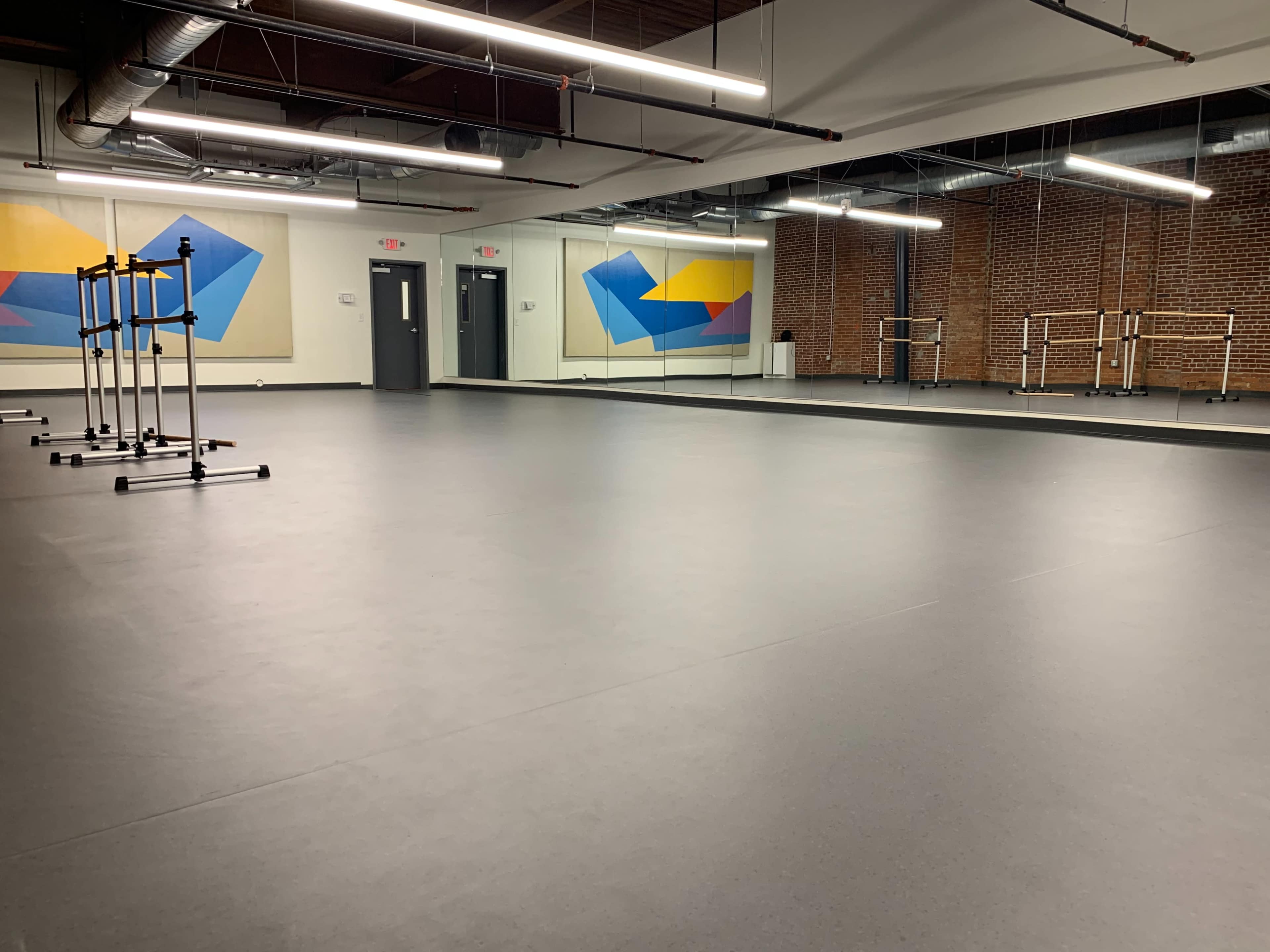A spacious dance studio with a smooth black floor, mirrored walls, and colorful abstract artwork on the back wall.