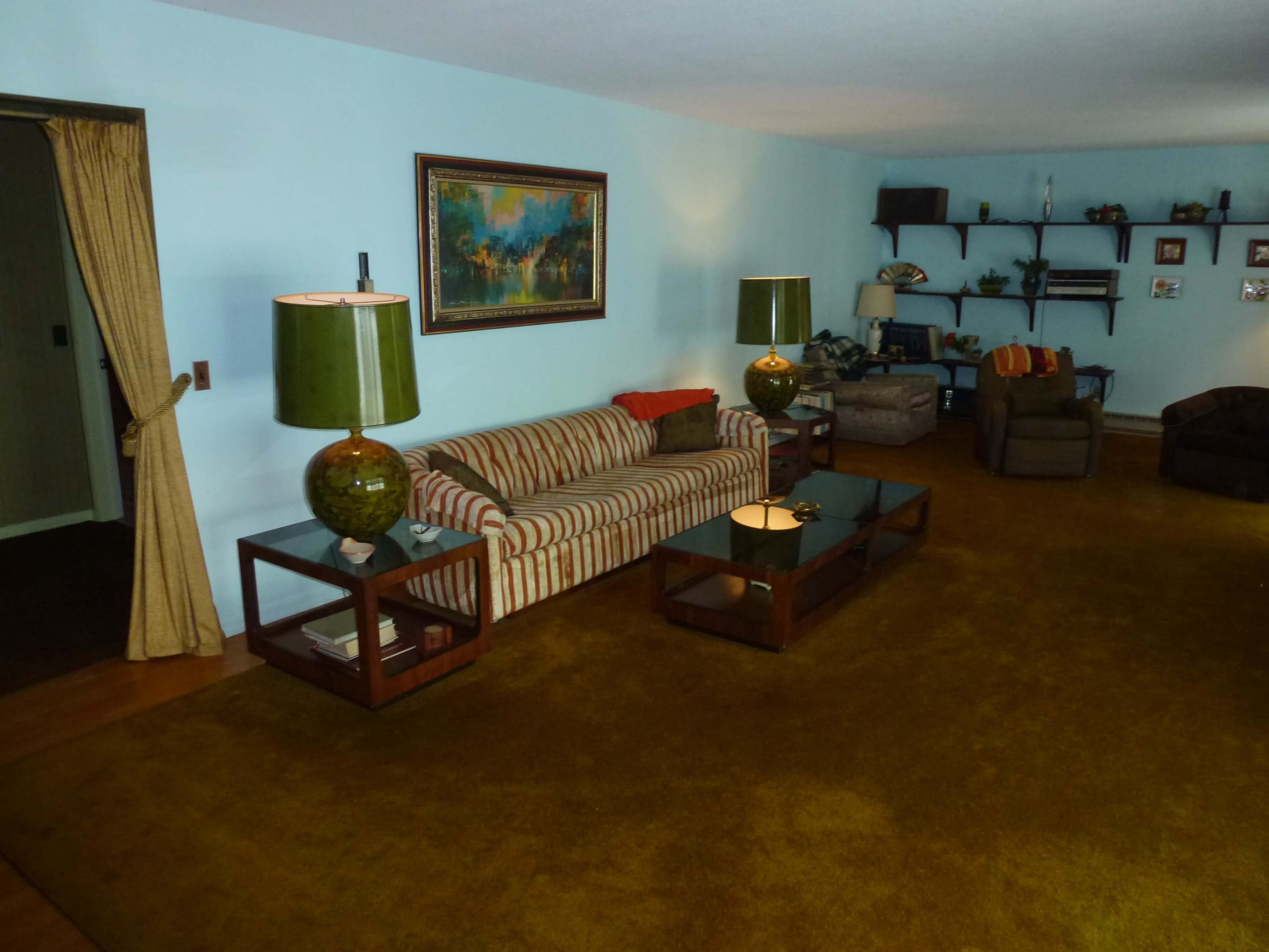 The image shows a living room with a striped sofa, green lamps on side tables, and a carpeted floor.