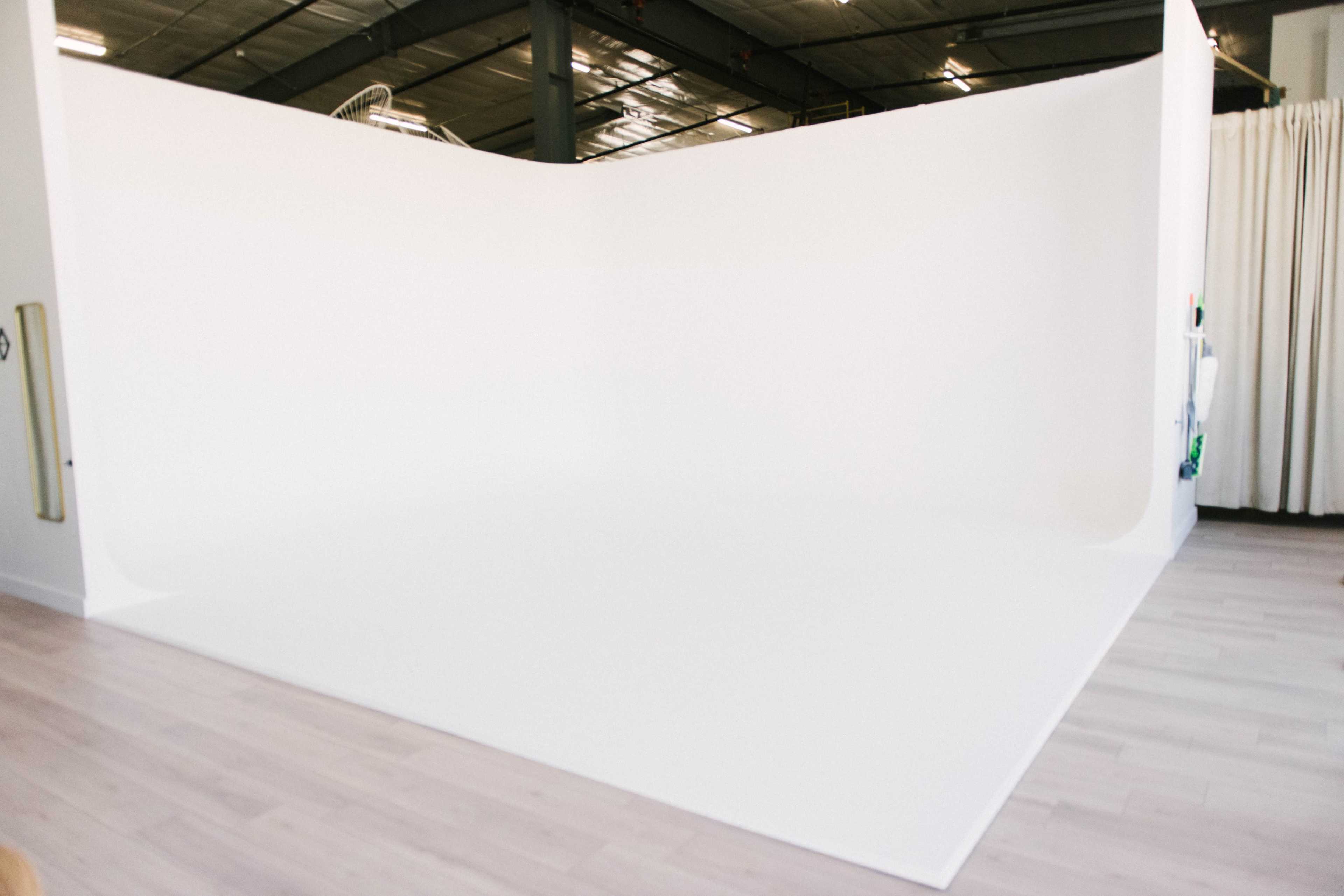 A spacious photography studio with a seamless white backdrop and light-colored wooden flooring.