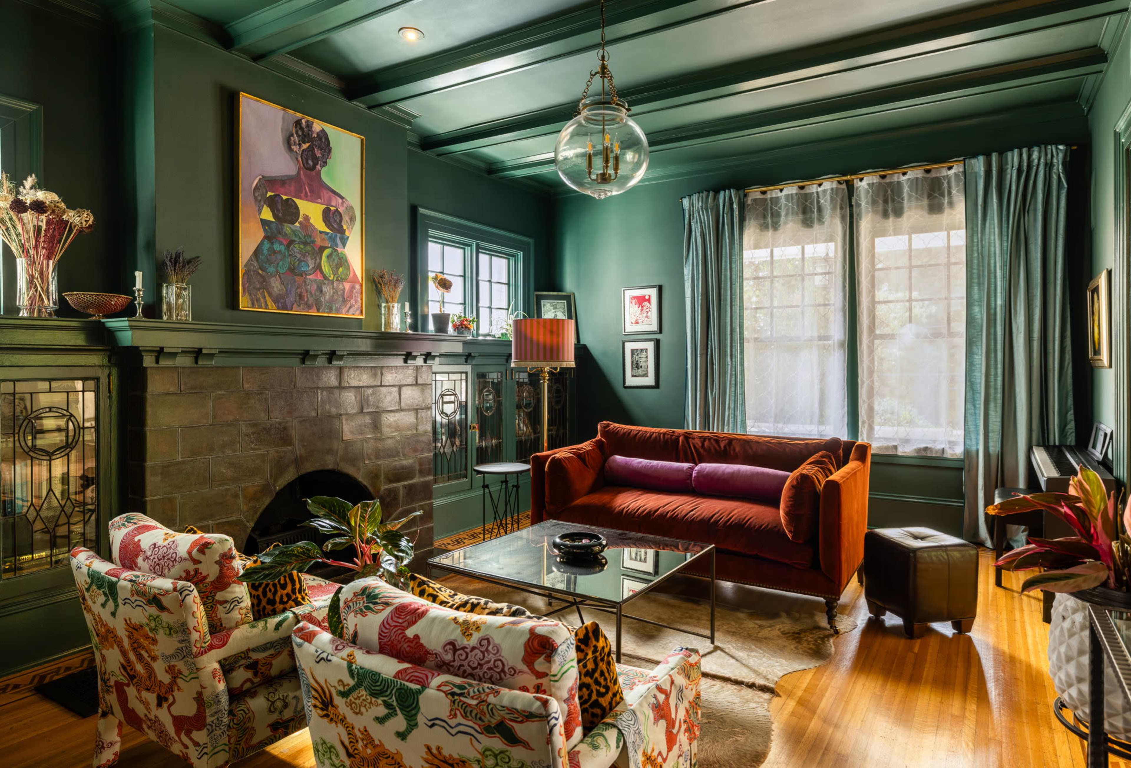 The image shows a decorative living room featuring a colorful sofa, patterned chairs, a coffee table, and a fireplace, with artwork and plants enhancing the space.