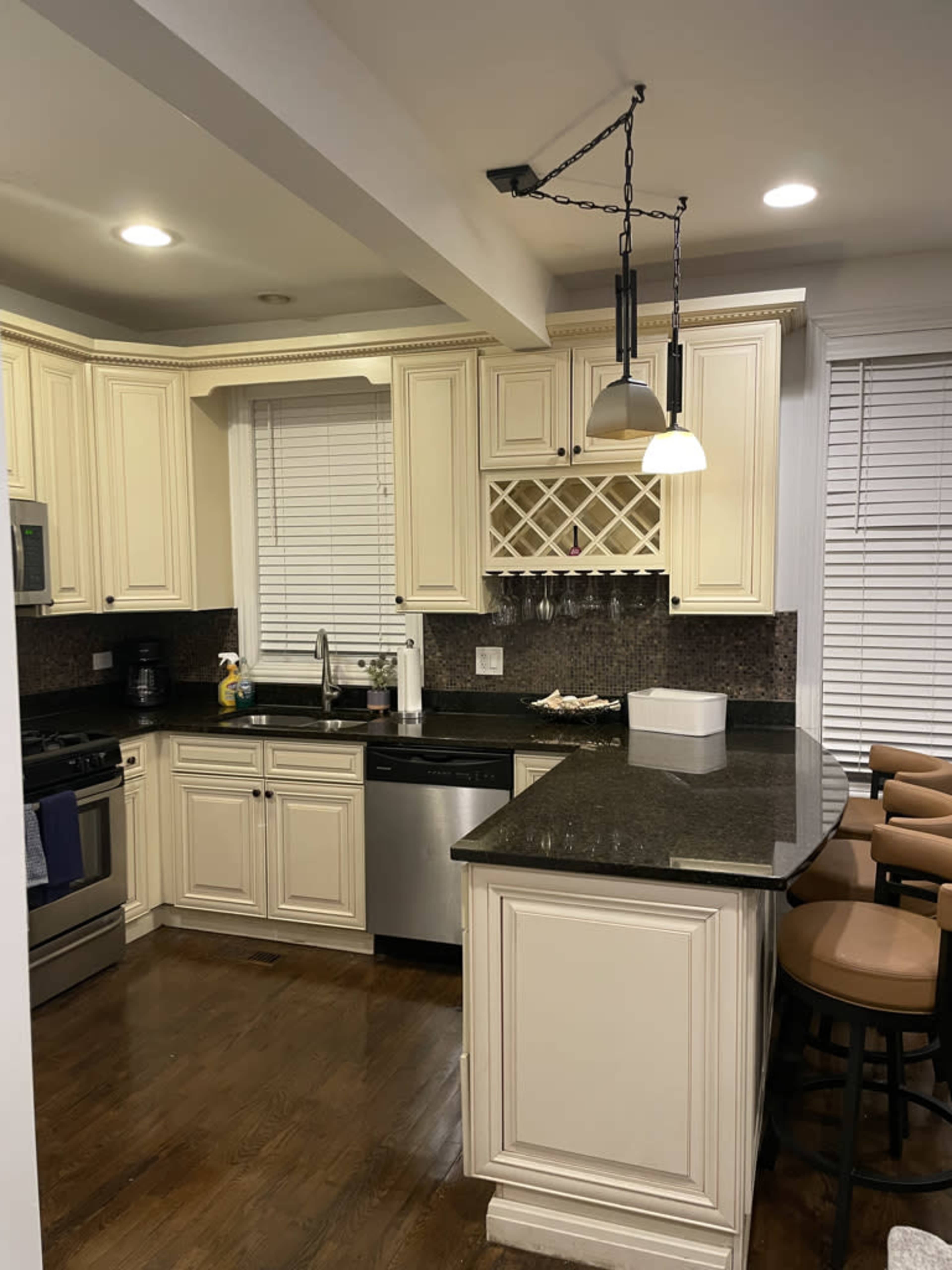 A kitchen with cream-colored cabinets, a dark granite countertop, and a breakfast bar with high stools.