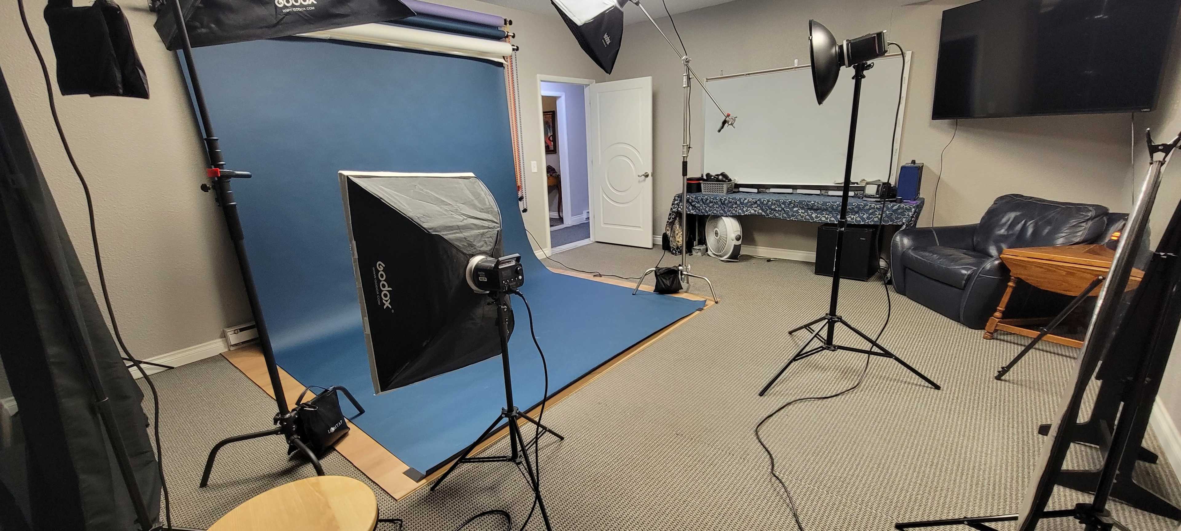 A photography studio setup with blue backdrop, lighting equipment, and furniture arranged in the room.