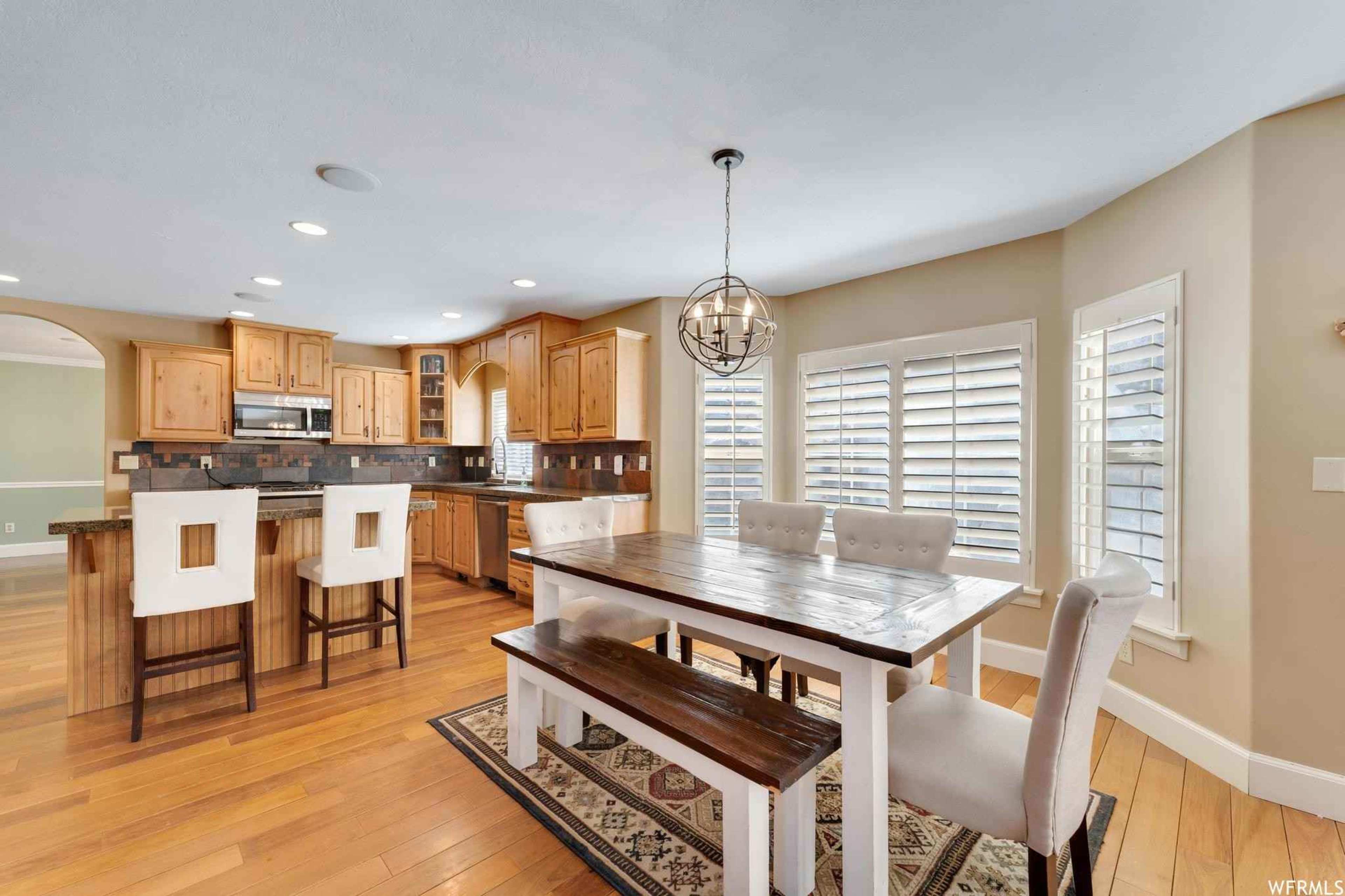 A modern kitchen with wooden cabinets, a central island, and a dining area featuring a large wooden table surrounded by upholstered chairs.