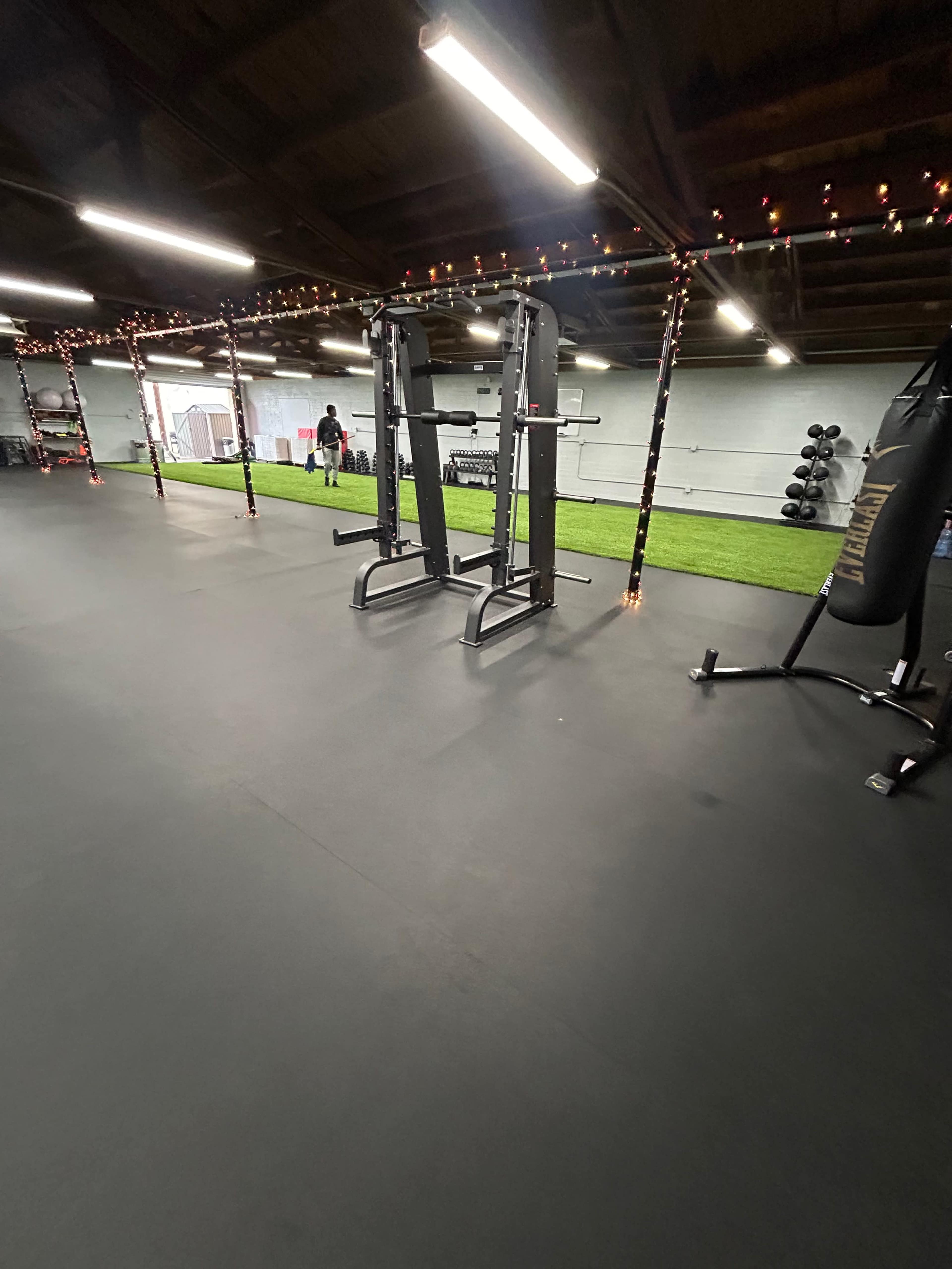 A spacious gym area with two weightlifting machines, artificial grass flooring, and a boxing bag in the corner.