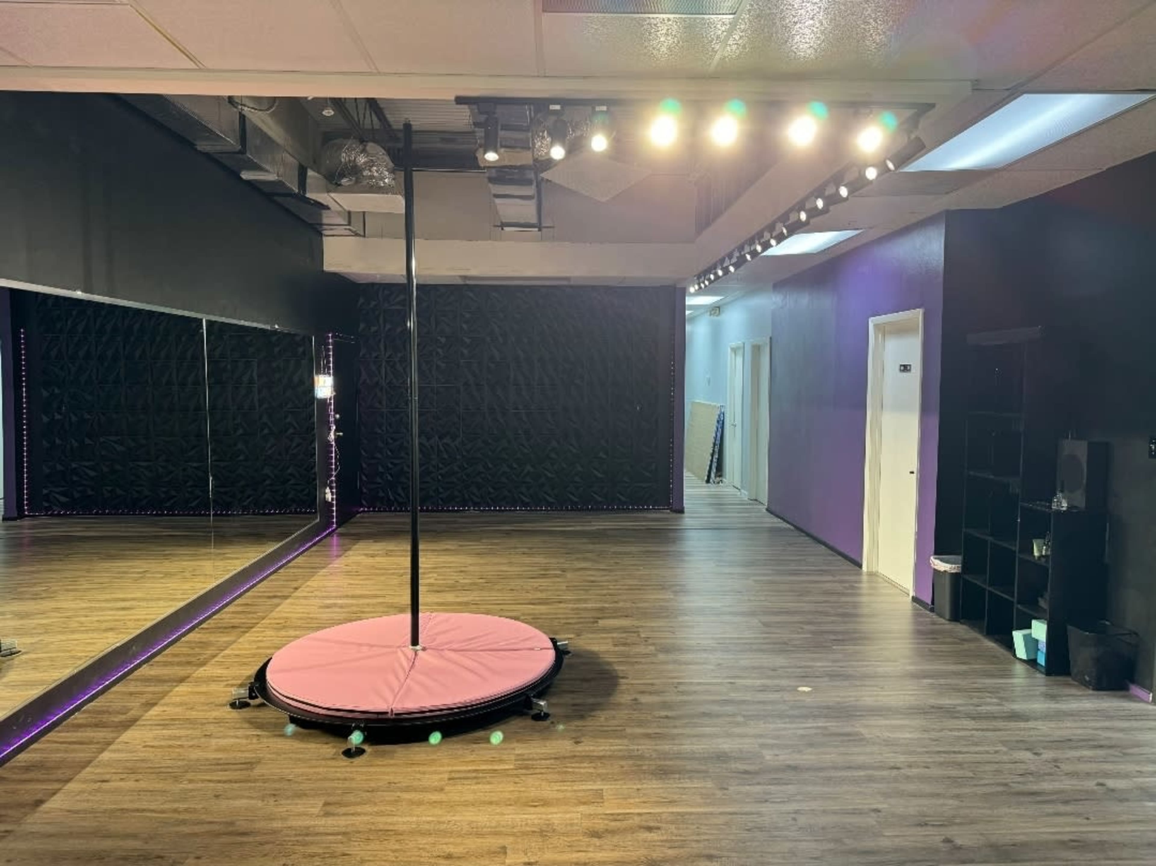 An empty dance studio with a central pole, mirrored walls, and hardwood flooring.
