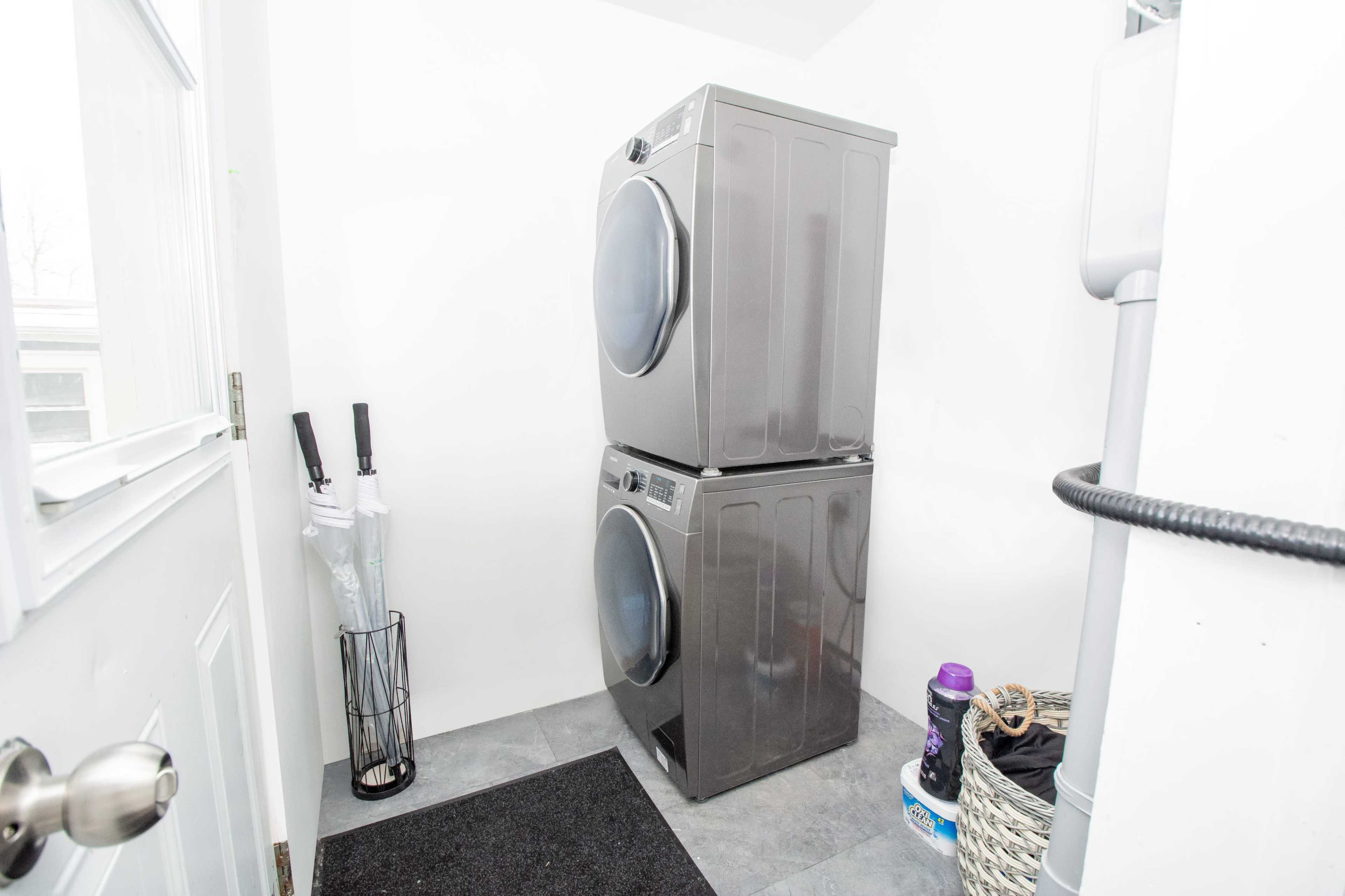 A stacked washer and dryer in a small laundry area, alongside umbrellas and a basket on the floor.