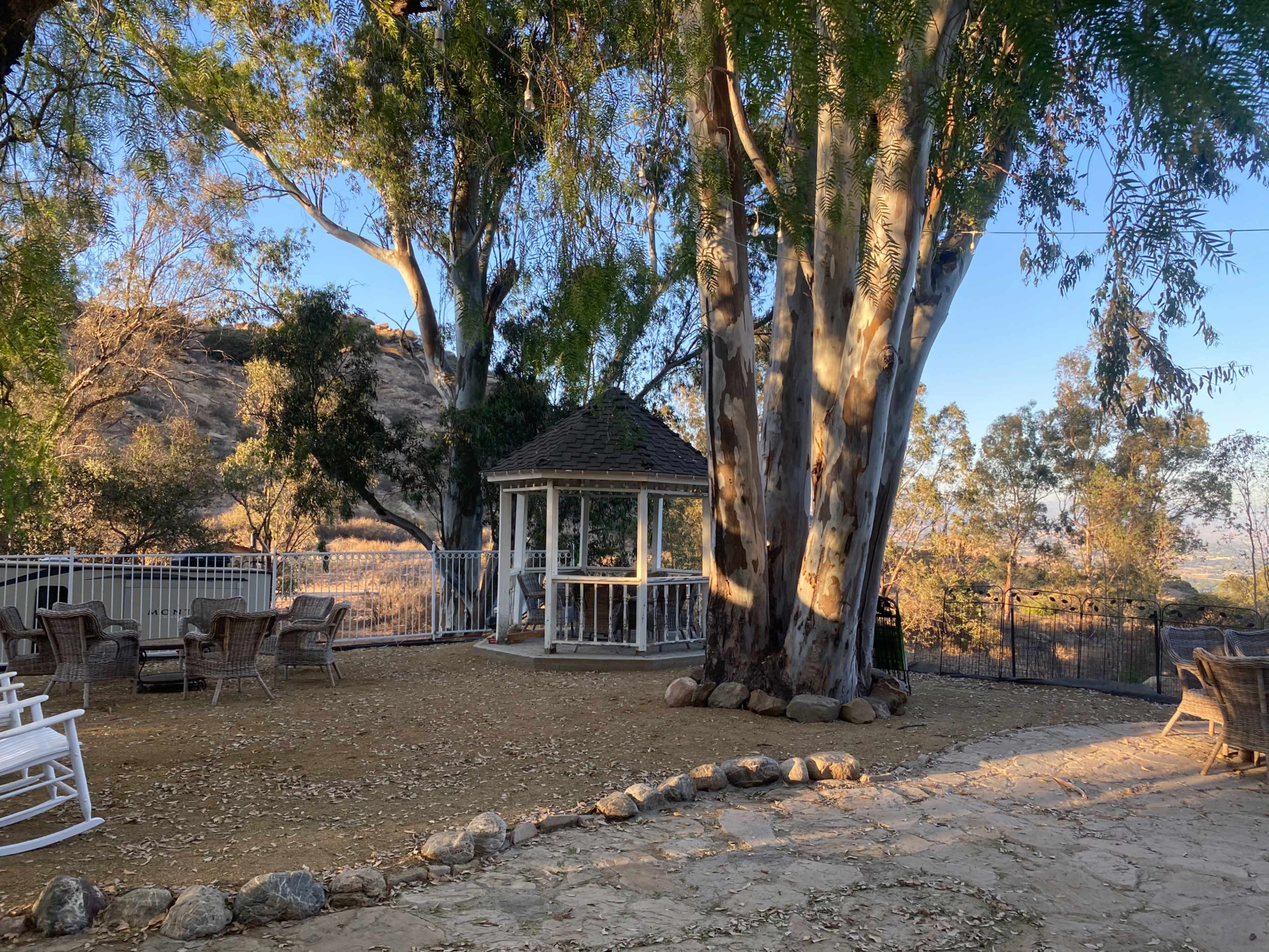 A gazebo is surrounded by large trees and a rocky pathway in a landscaped outdoor area.