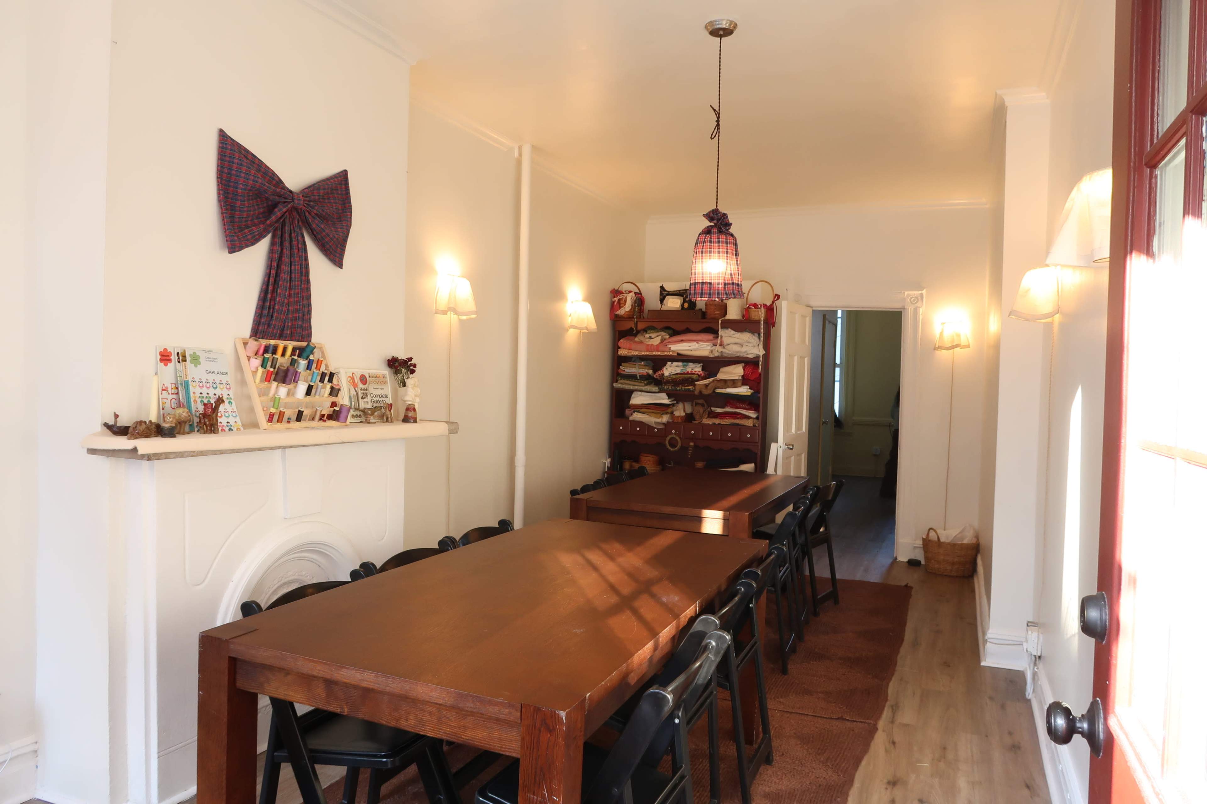 A long wooden table with chairs is positioned in a well-lit dining room adorned with decorative wall items and a shelf filled with various objects.