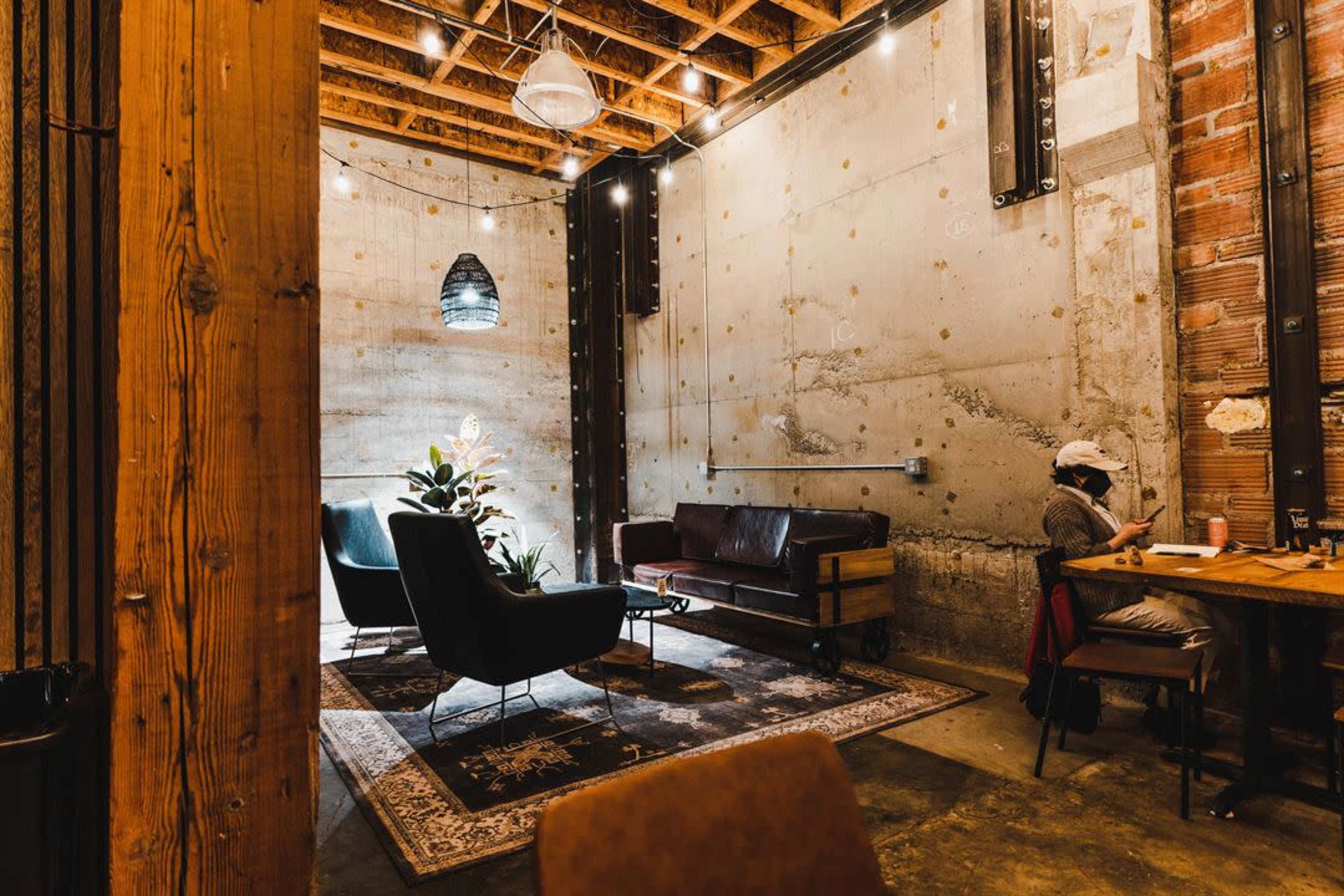 A cozy interior of a café with industrial design elements, featuring a mix of seating options, potted plants, and warm lighting.