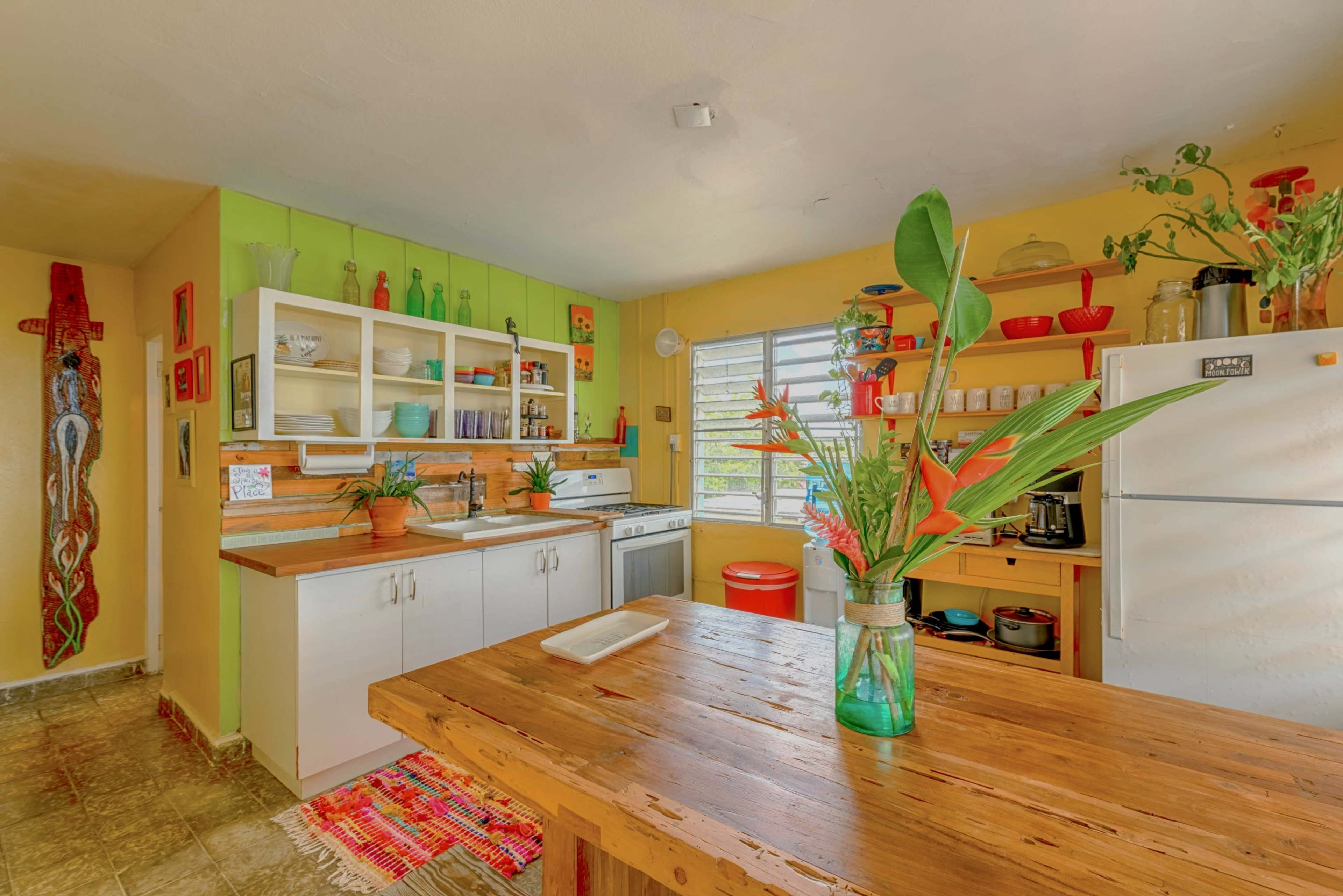 The kitchen features wooden countertops, white cabinetry, and vibrant green and yellow walls, adorned with houseplants and colorful decor.
