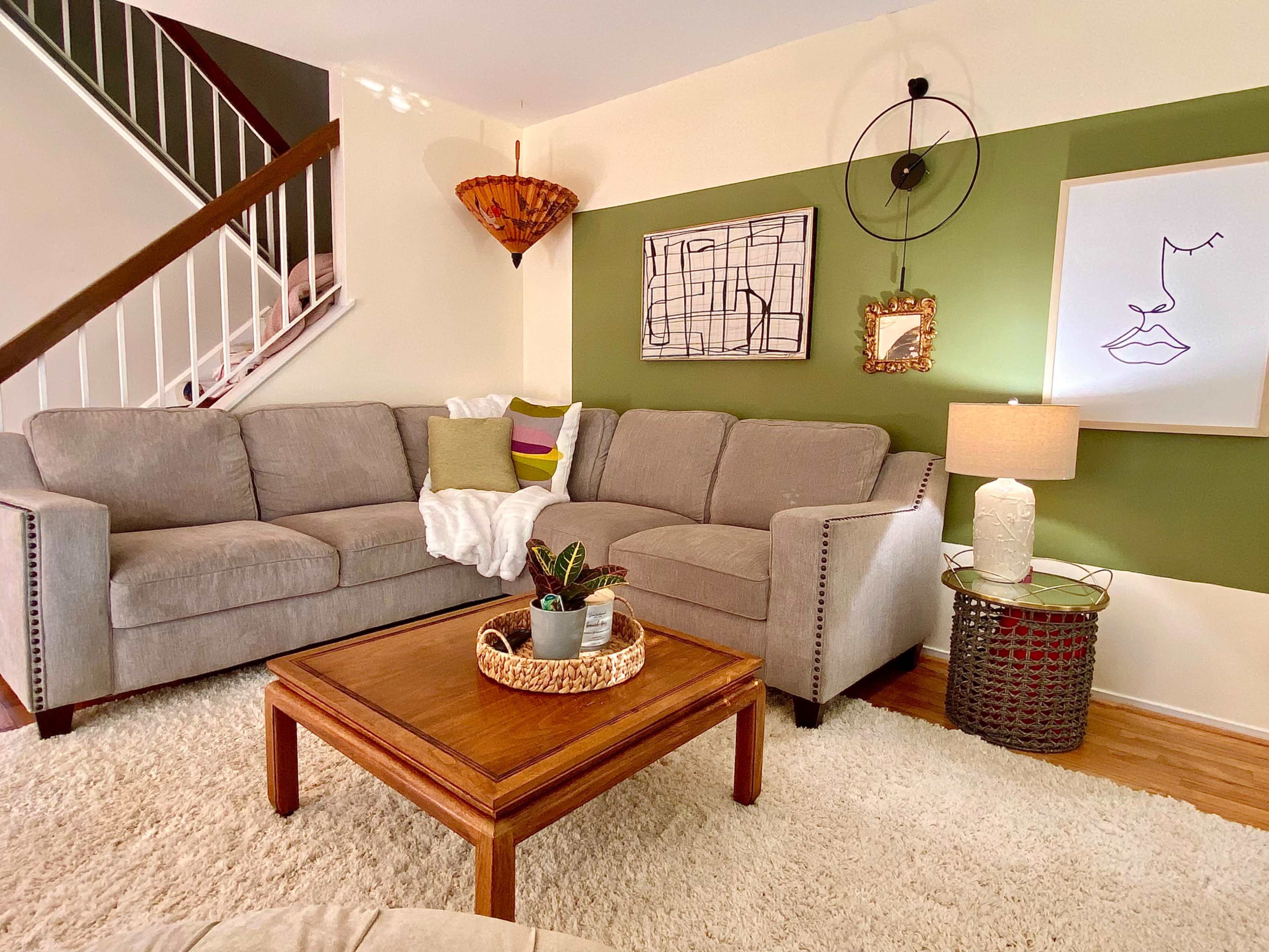 A cozy living room with a gray sectional sofa, a wooden coffee table, a soft rug, and various decorative elements on the walls and table.