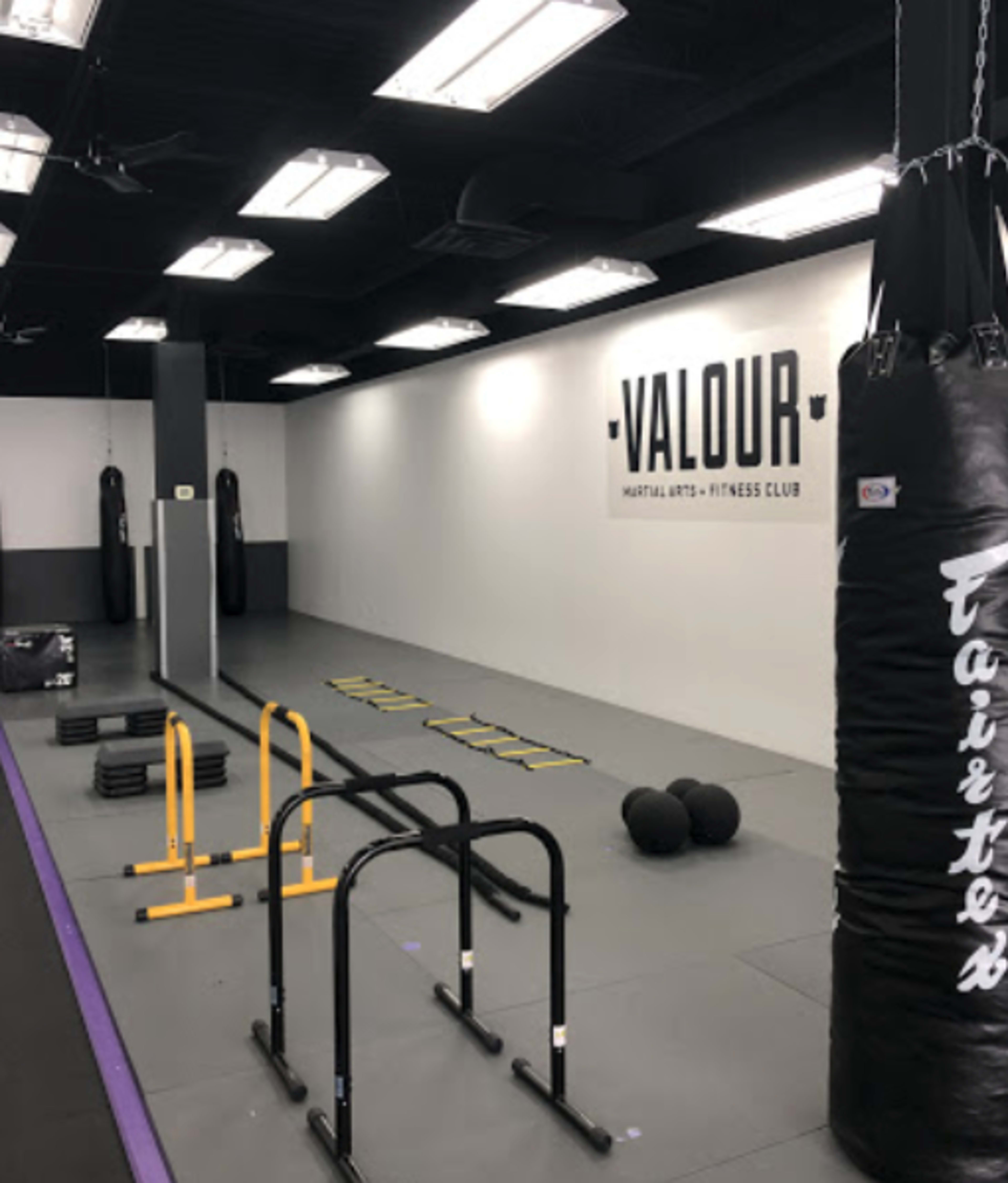 A fitness gym with a punching bag, agility training equipment, and a wall displaying the word "VALOUR."