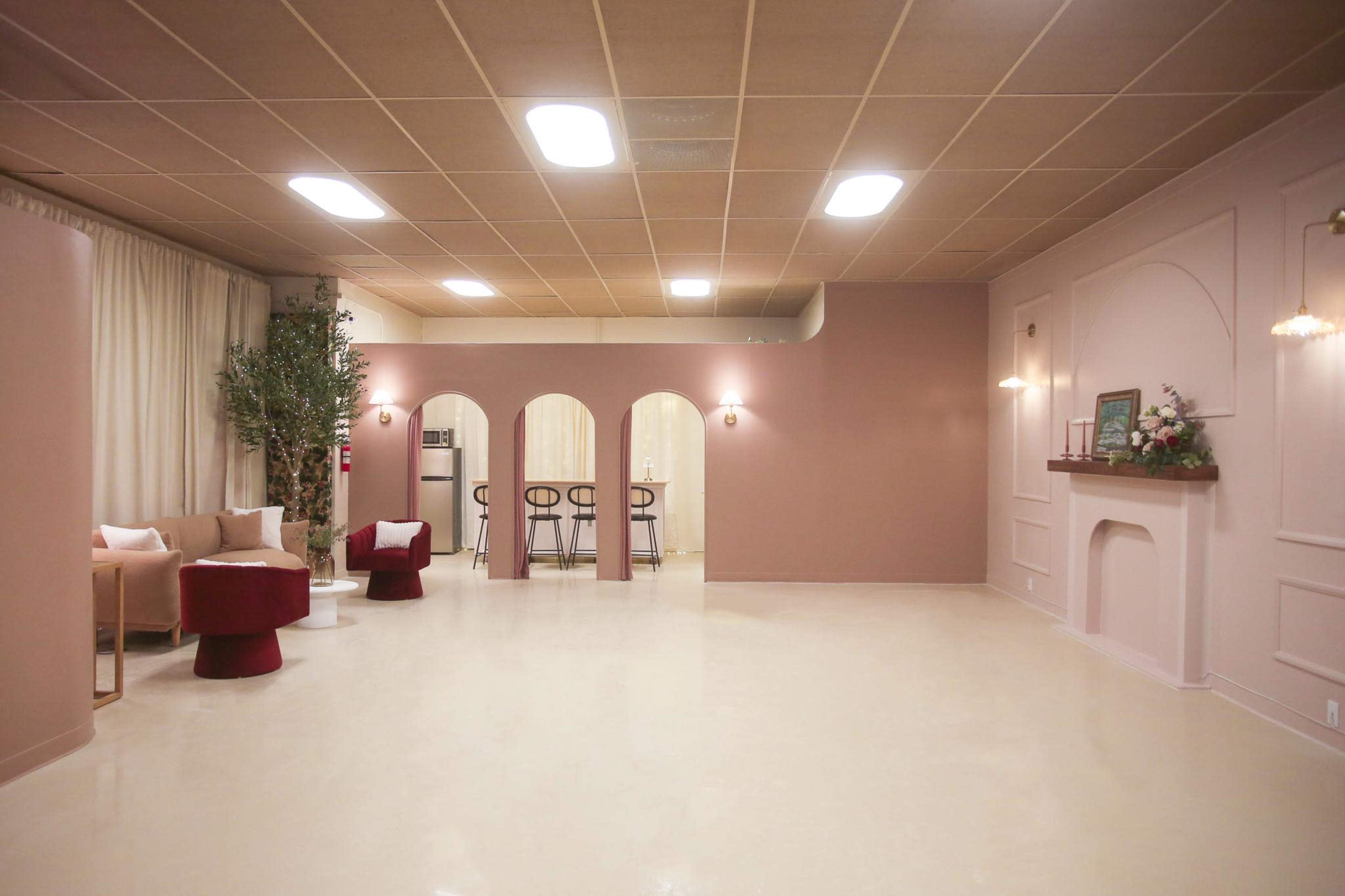 A spacious, modern interior with a light-colored floor, beige and pink walls, and a seating area that includes chairs and small tables.