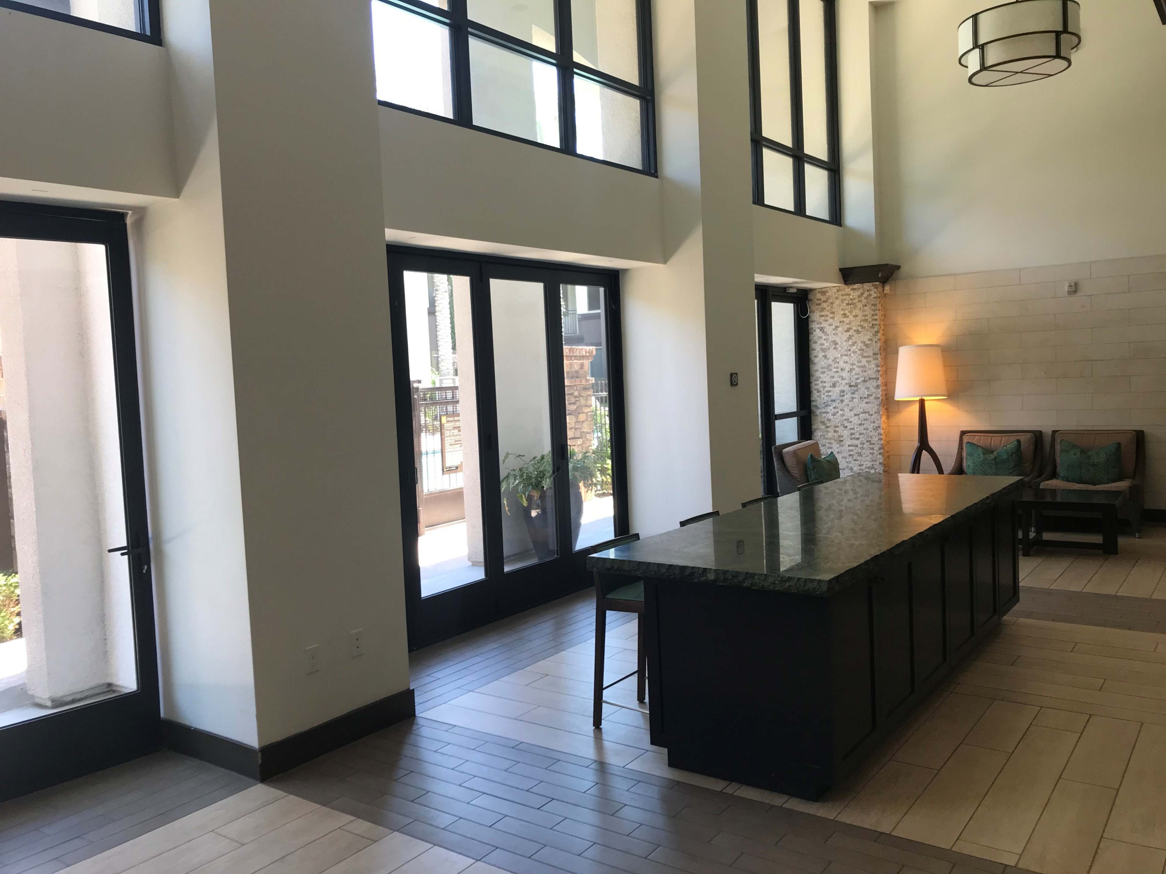 A modern lobby with large windows, a dark countertop island, and a few chairs arranged near a lamp.