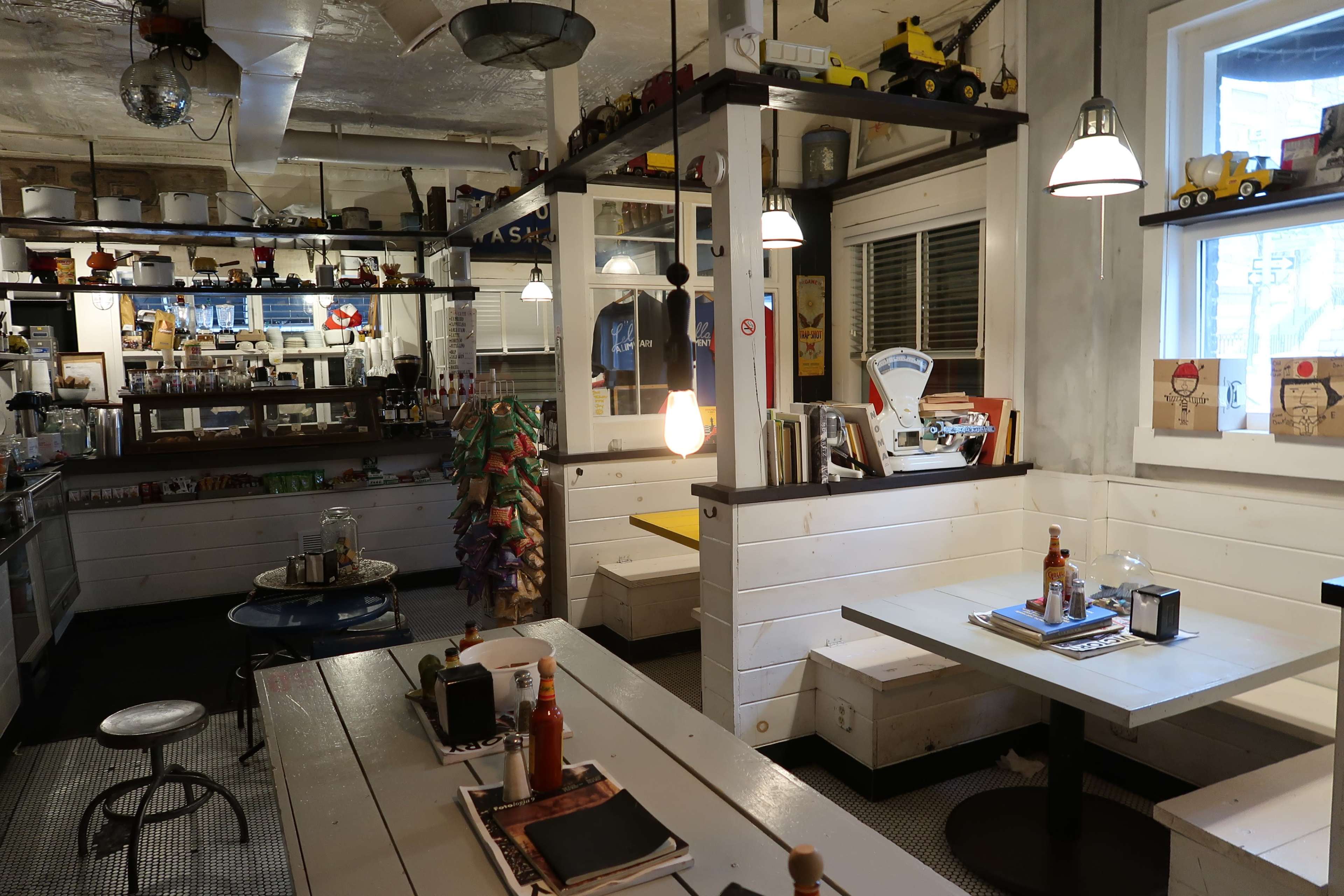 A modern diner interior with wooden tables, white benches, and decorative items on shelves and walls.