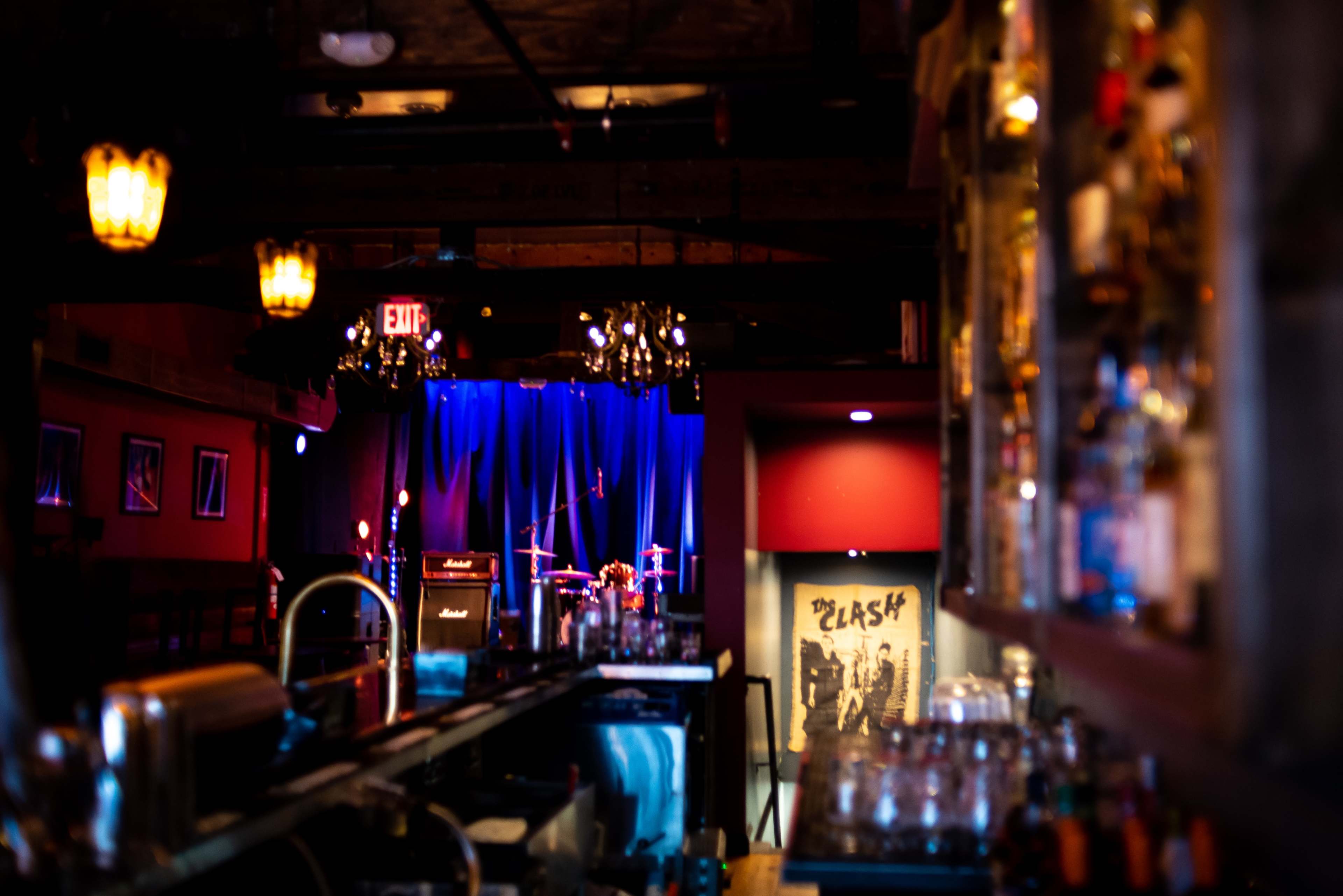 The interior of a bar features a dimly lit stage with musical instruments and a bar counter lined with glassware.