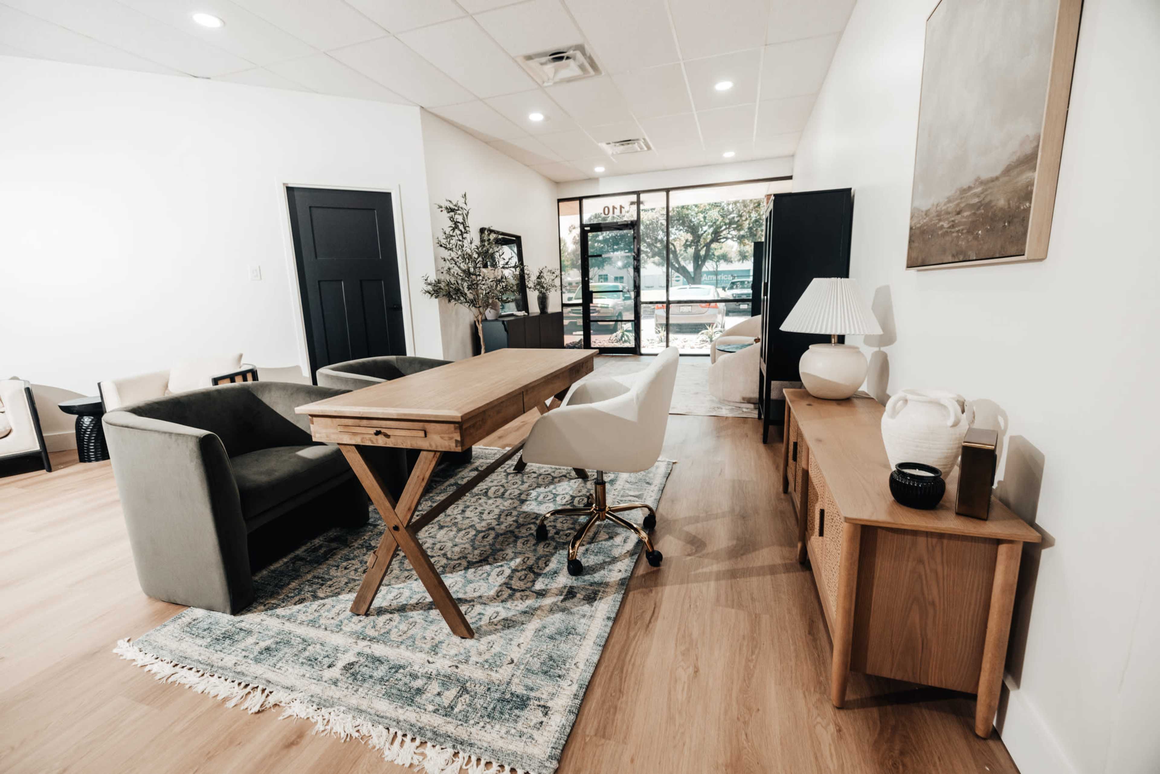 A modern office space with a wooden table, two chairs, and a console table, complemented by a large window overlooking an outdoor area.