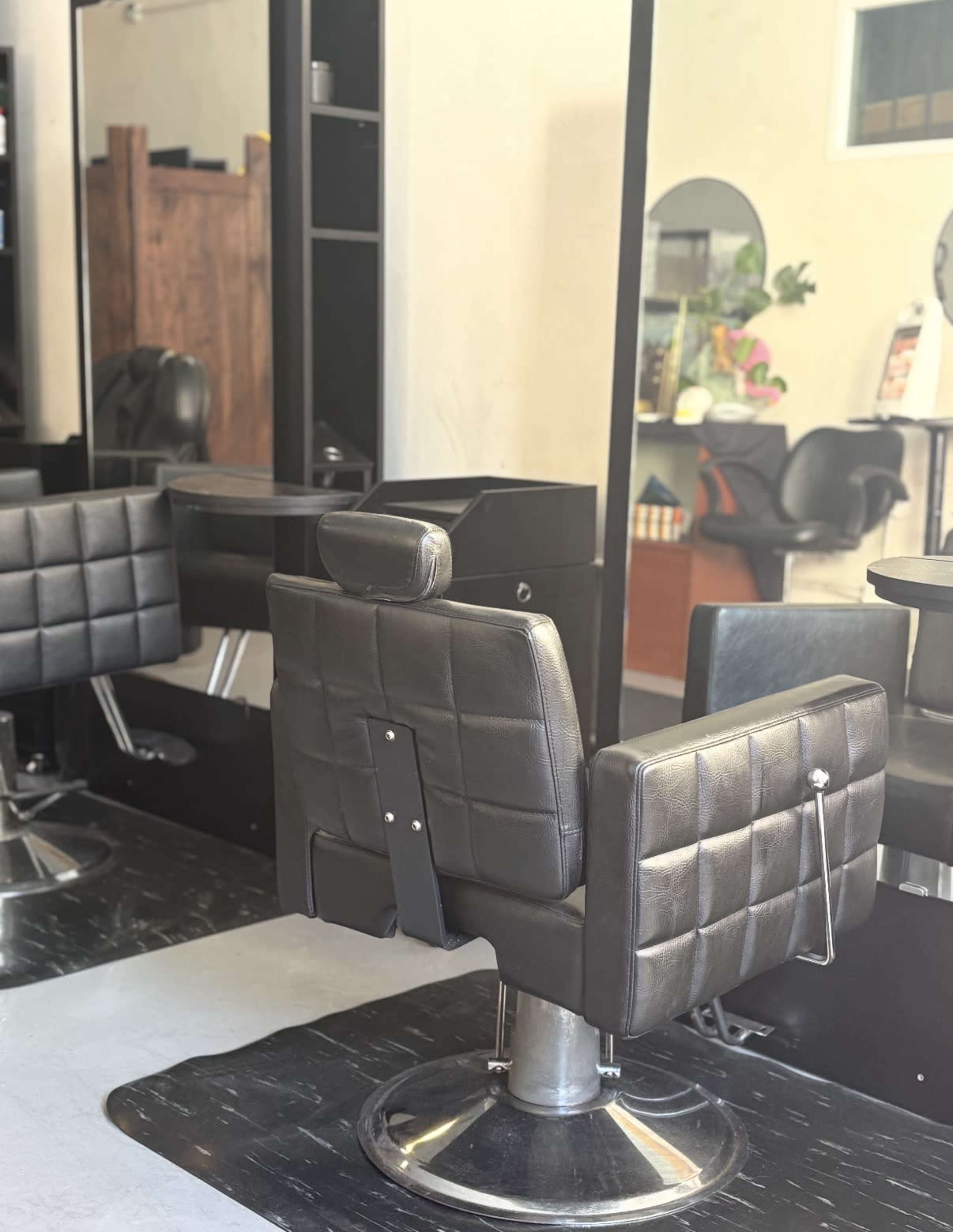 The image shows a modern hair salon interior featuring a black styling chair and mirrors against a minimalist backdrop.