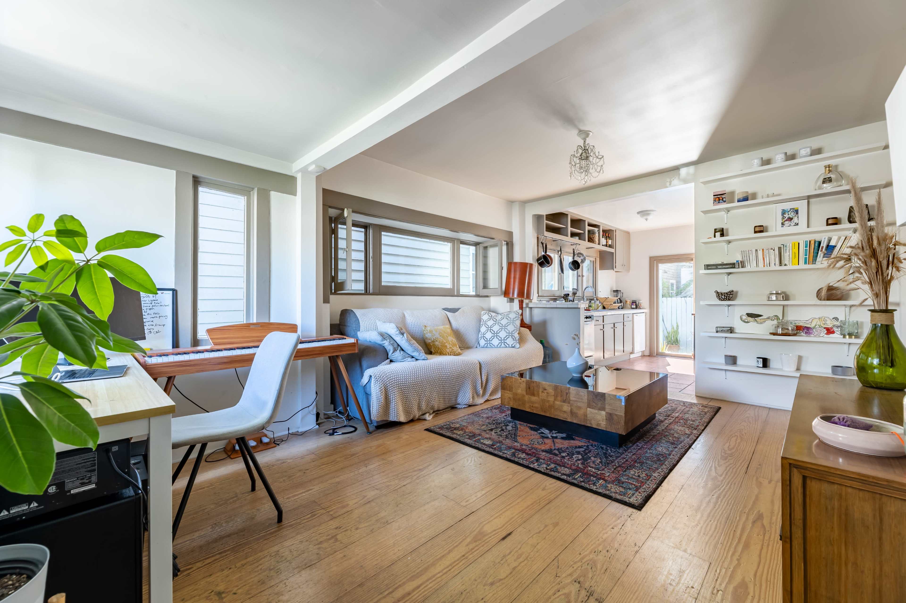 A modern living room with a sofa, a coffee table, and wooden flooring, featuring a keyboard on the side and shelves filled with books and decorative items.