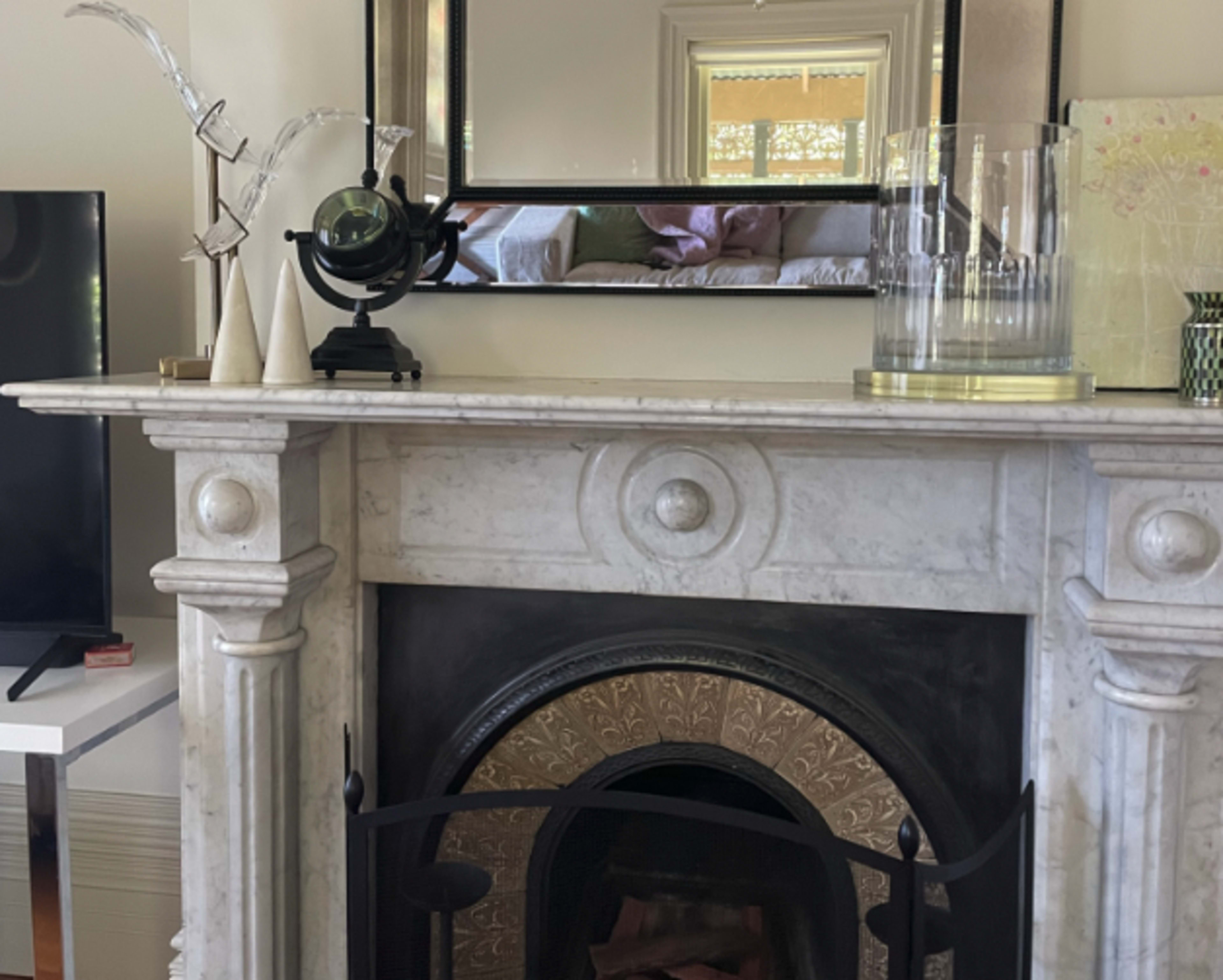 A marble fireplace with an ornate fire grate, a decorative mirror above it, and various decorative objects on the mantel.