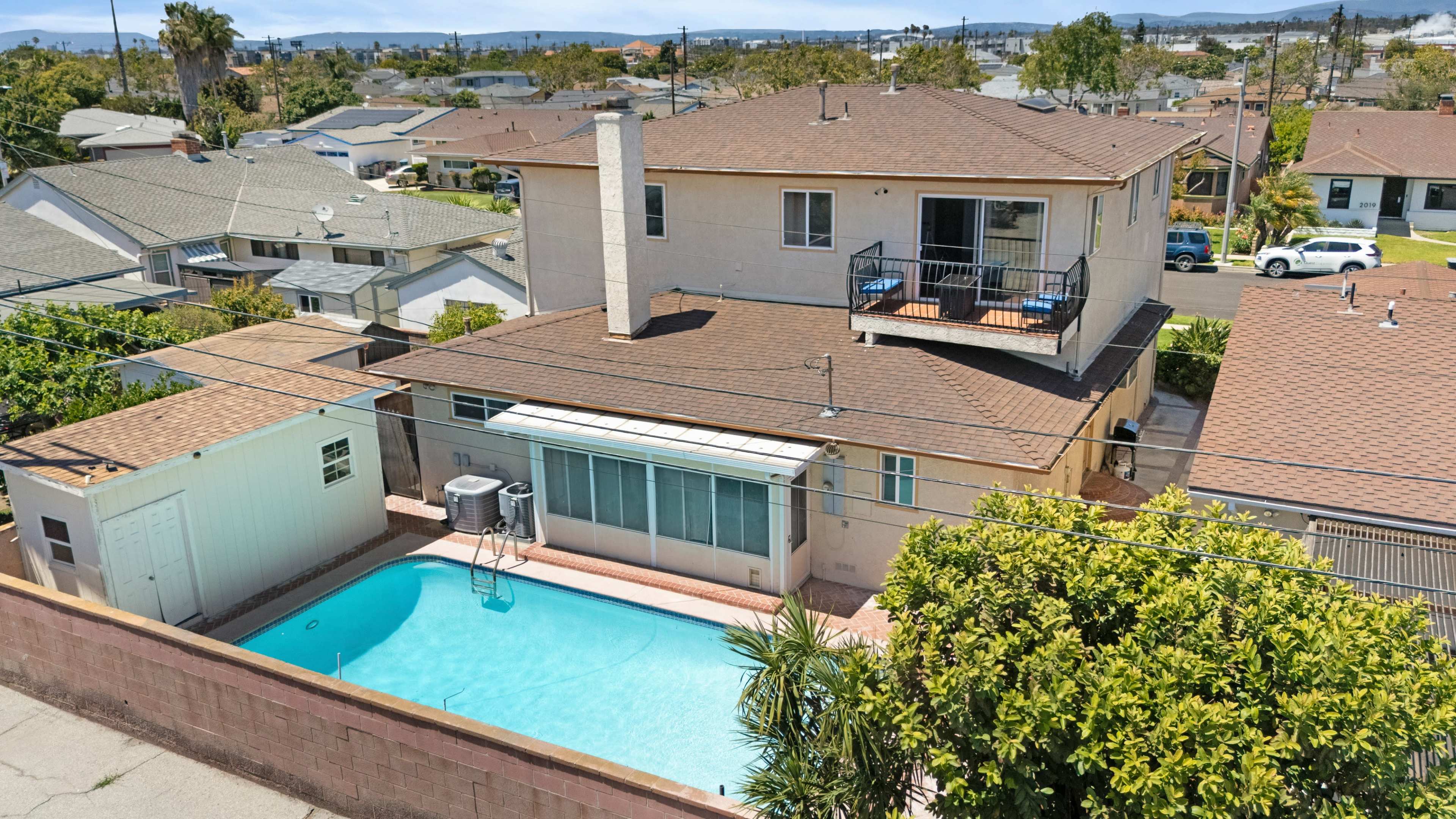 The image shows a residential backyard featuring a swimming pool, a two-story house with a balcony, and surrounding landscaping.