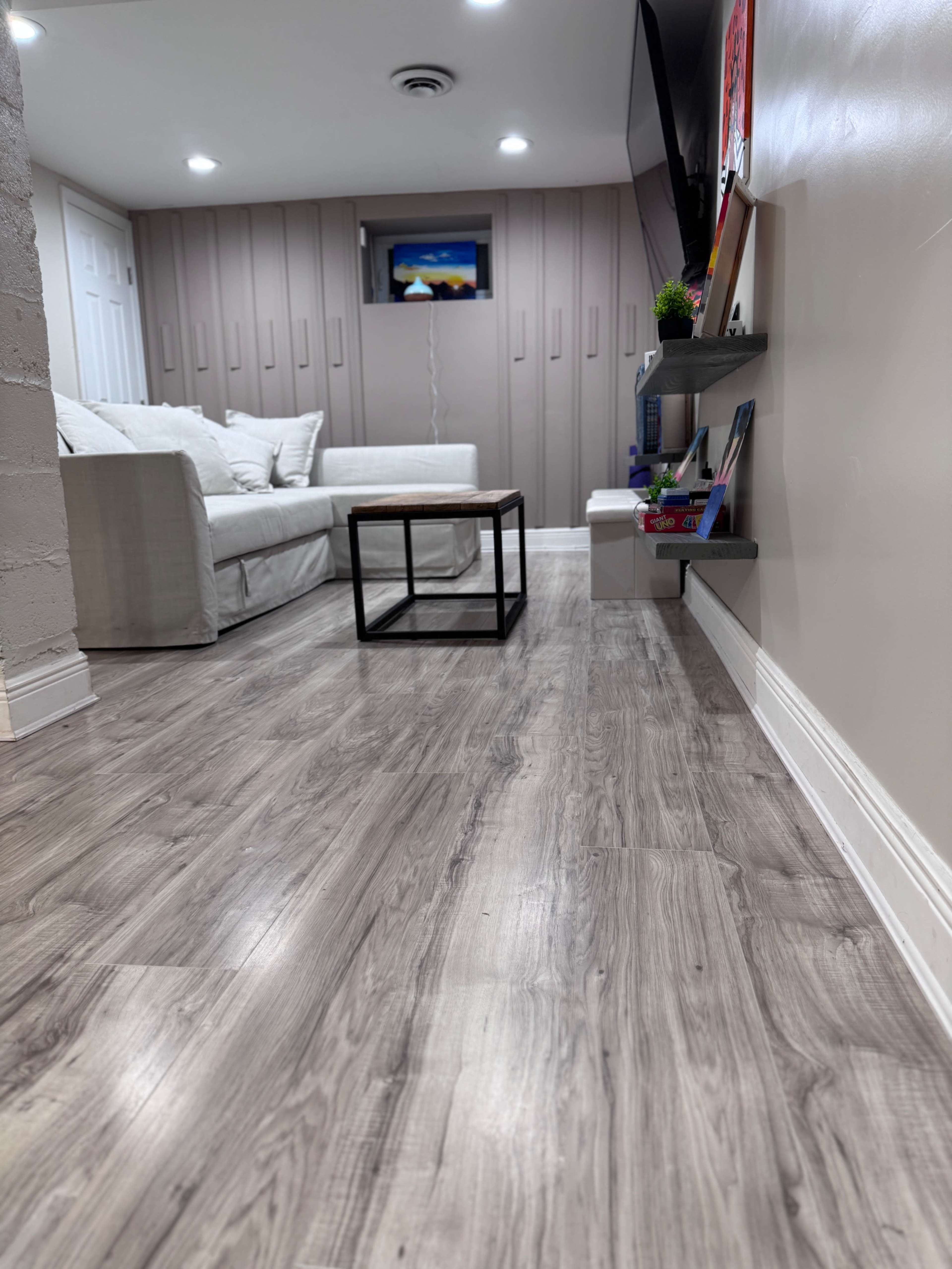 The image shows a modern living room with a light-colored couch, a coffee table, and a mounted television on the wall.