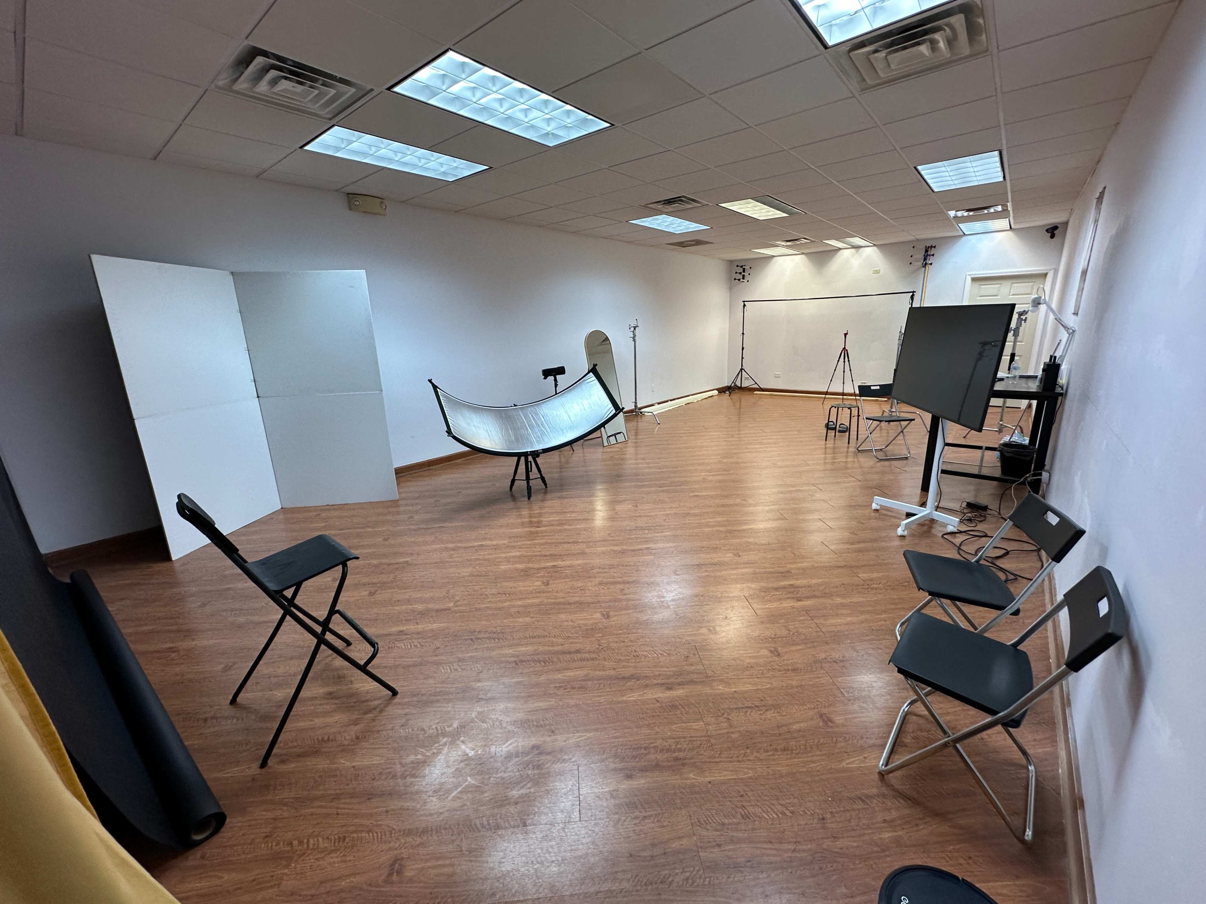A spacious, empty studio with wooden flooring, several photography backdrops, and various equipment set up for shoots.