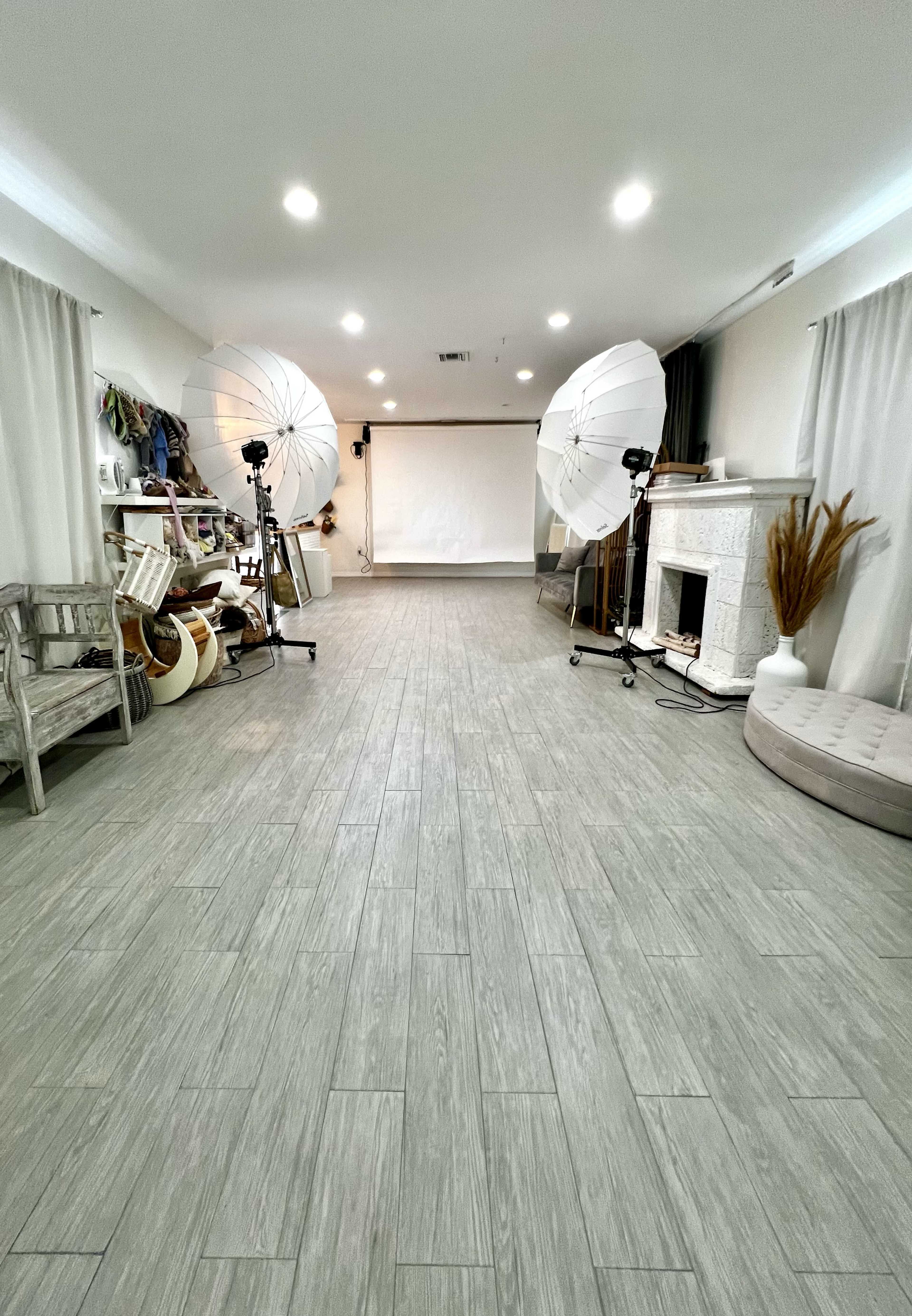 The image shows an empty studio space with a backdrop, two lighting setups, a decorative fireplace, and various props arranged along one wall.