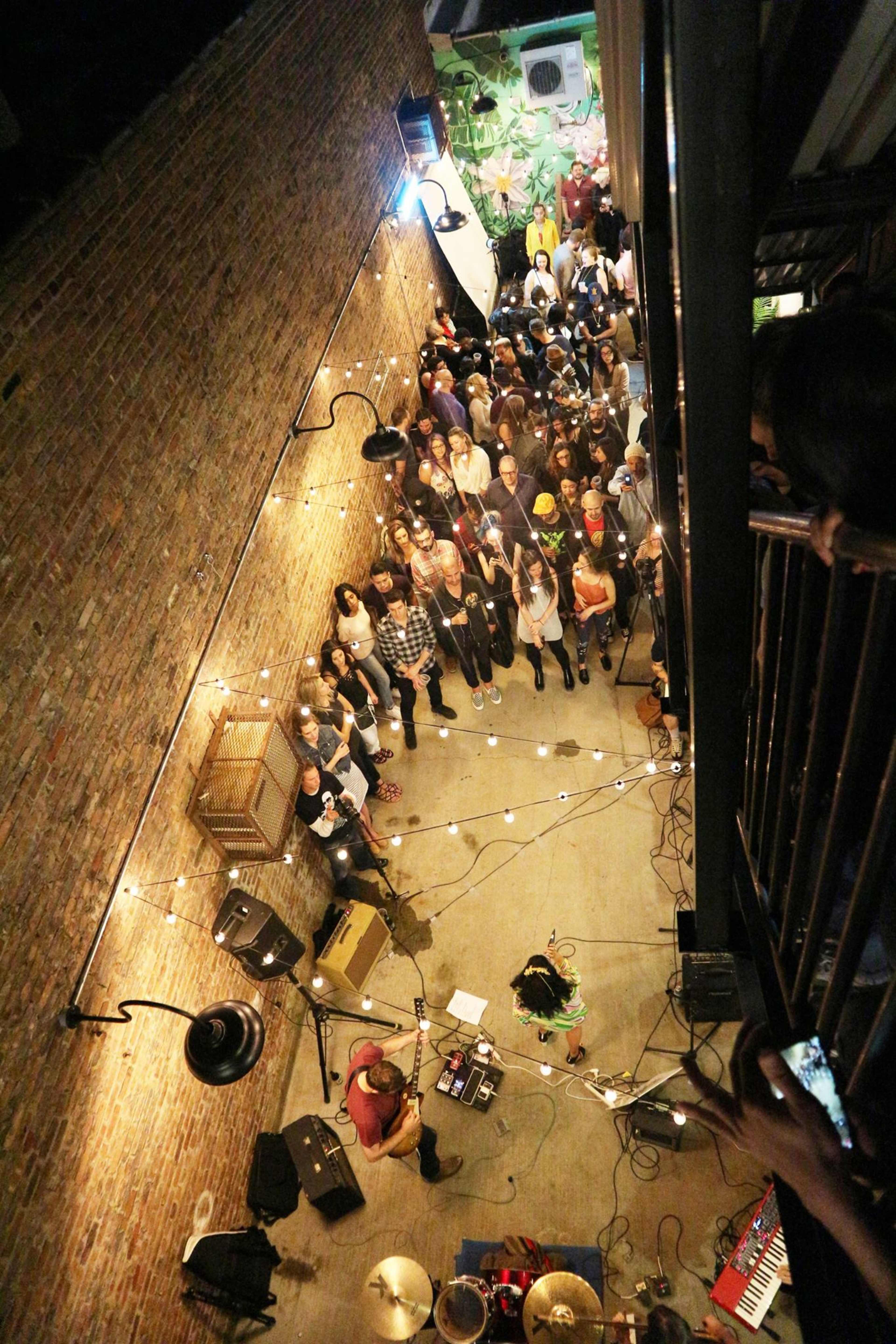 A crowd gathers in a rustic alleyway for a live music performance, illuminated by string lights.