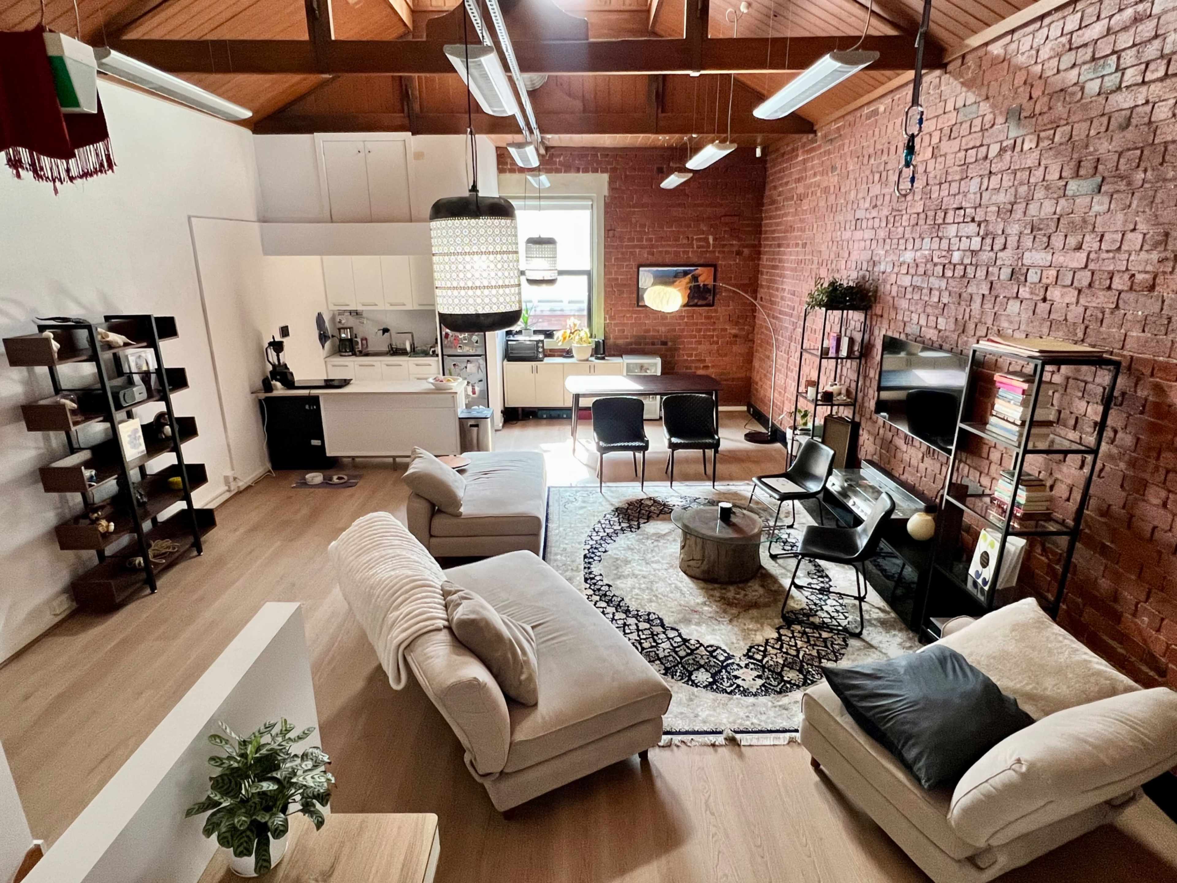 The image shows a modern living space featuring a cozy arrangement of furniture, including a large sectional sofa, a round coffee table, and a dining area with a kitchen in the background.