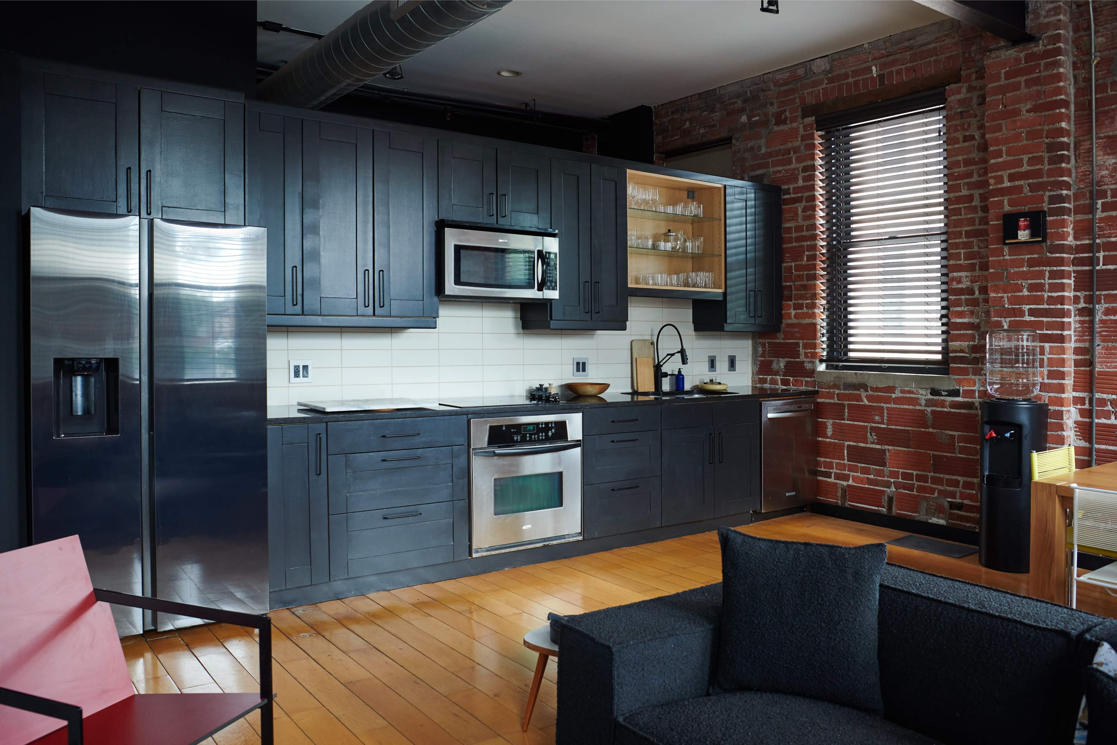 A modern kitchen featuring dark cabinetry, stainless steel appliances, and exposed brick walls.