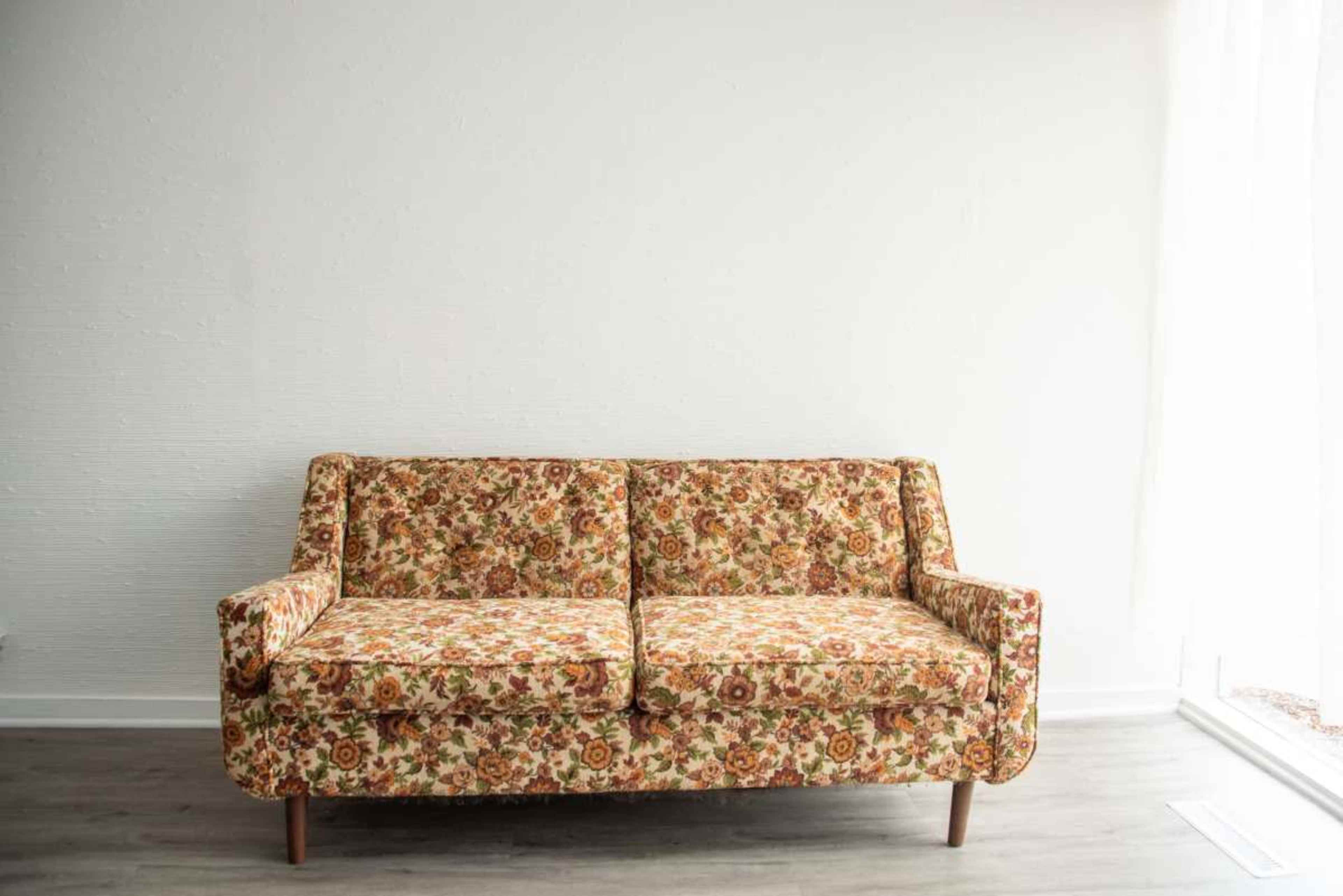 A floral-patterned sofa sits against a plain white wall in a well-lit room.