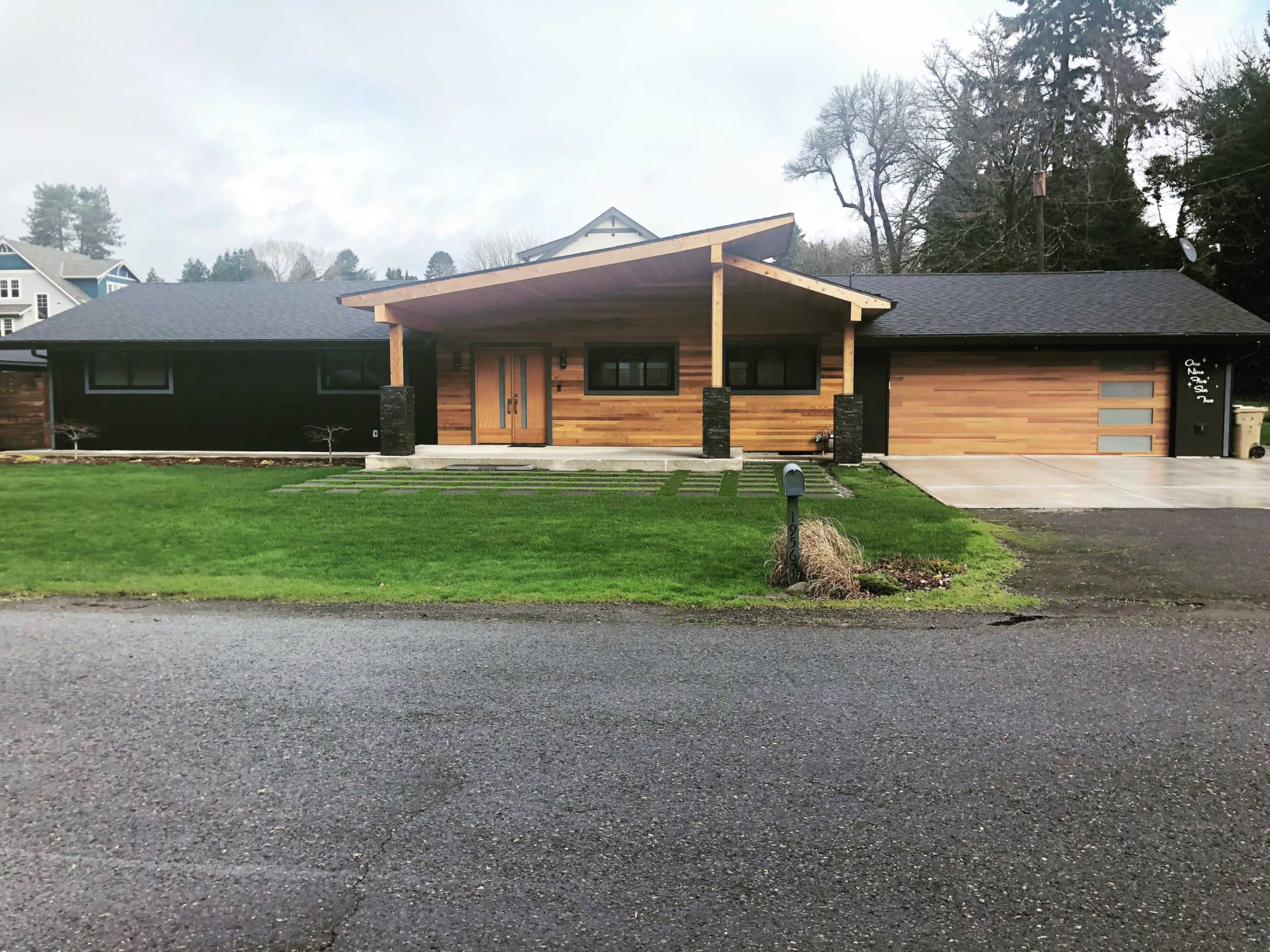 A modern single-story house with a wooden facade, a large front porch, and a neatly landscaped lawn.