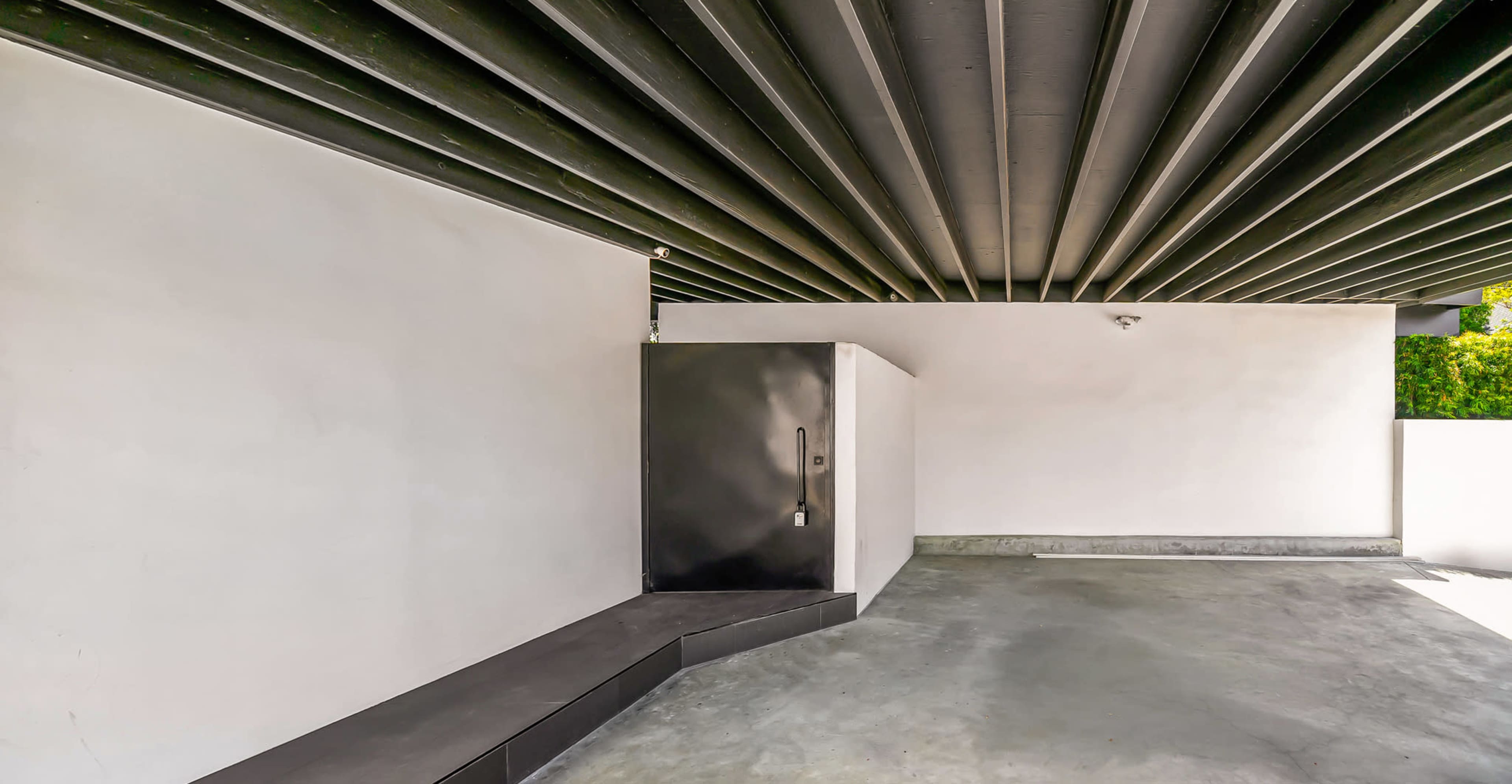 The image shows a modern, minimalist entryway with a black door and a concrete floor, framed by white walls and a slatted ceiling.
