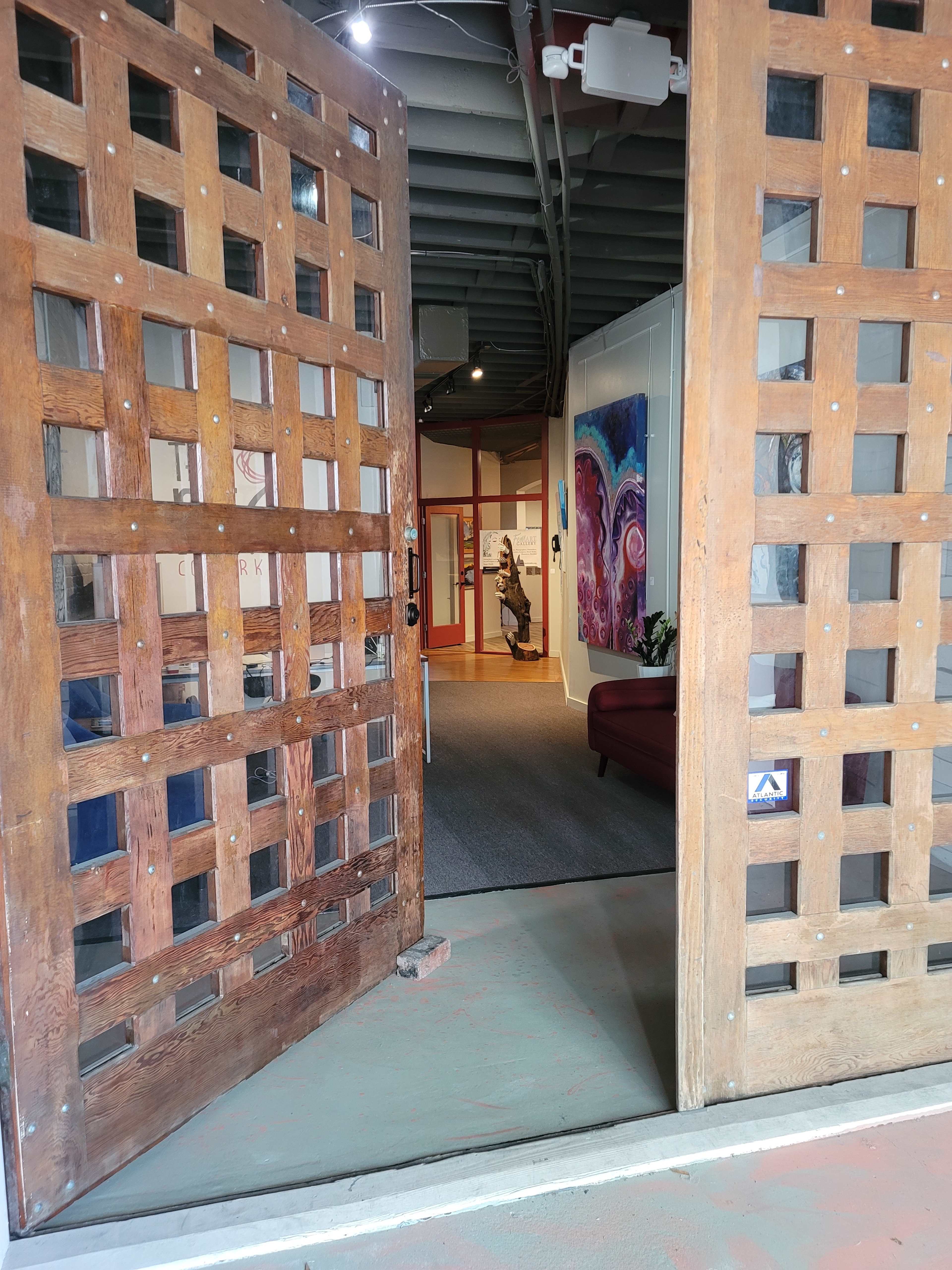 A pair of wooden double doors is open, revealing a hallway with artworks on the walls and a figure in the distance.