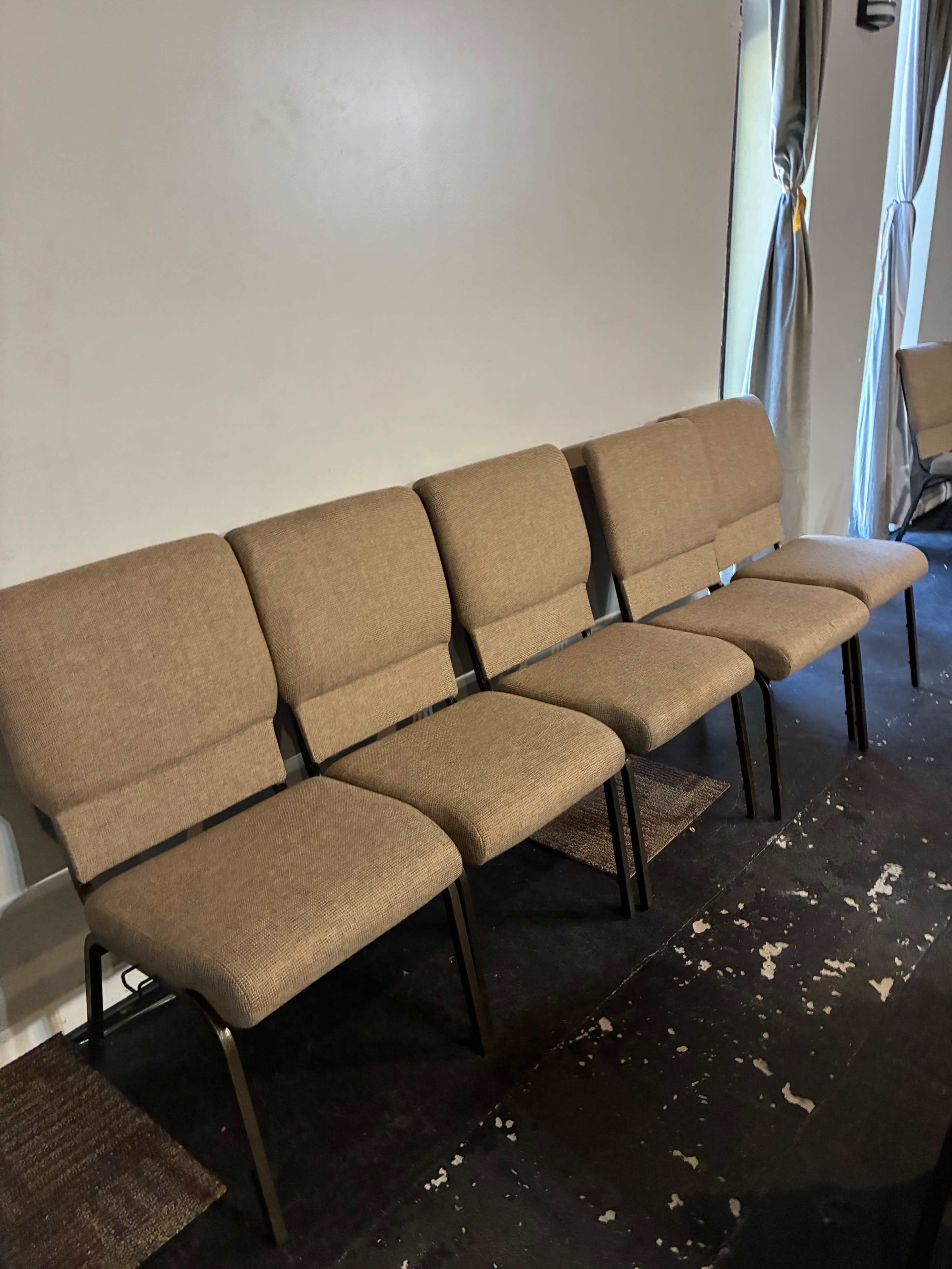 The image shows a row of five upholstered chairs with metal frames arranged against a wall in an indoor space.