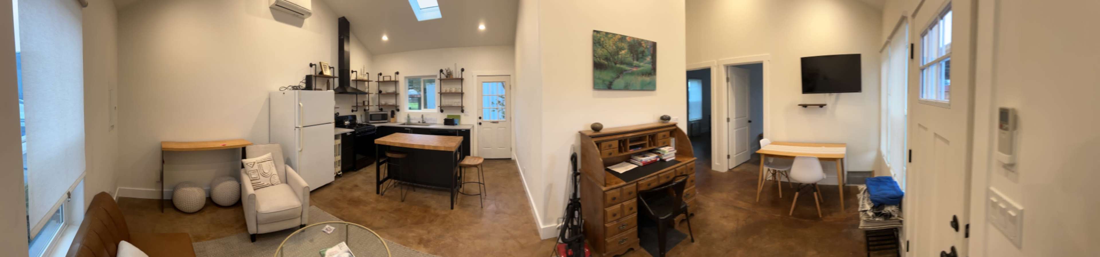A bright, open-concept living space featuring a kitchen, dining area, and cozy seating arrangement with a mix of furniture, including a wooden table and a vintage-style dresser.