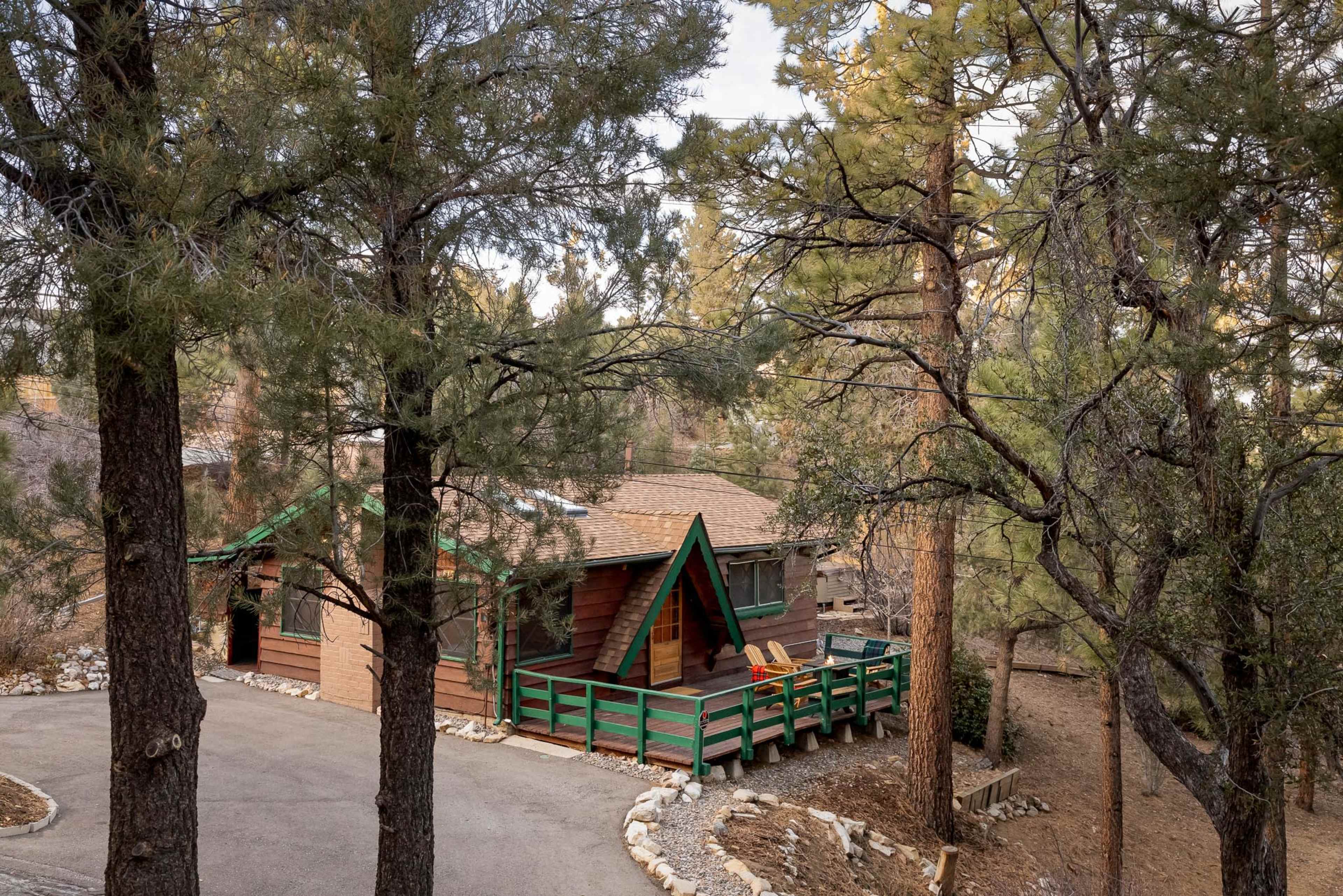 A wooden cabin with a green-trimmed porch sits among tall trees in a wooded area.