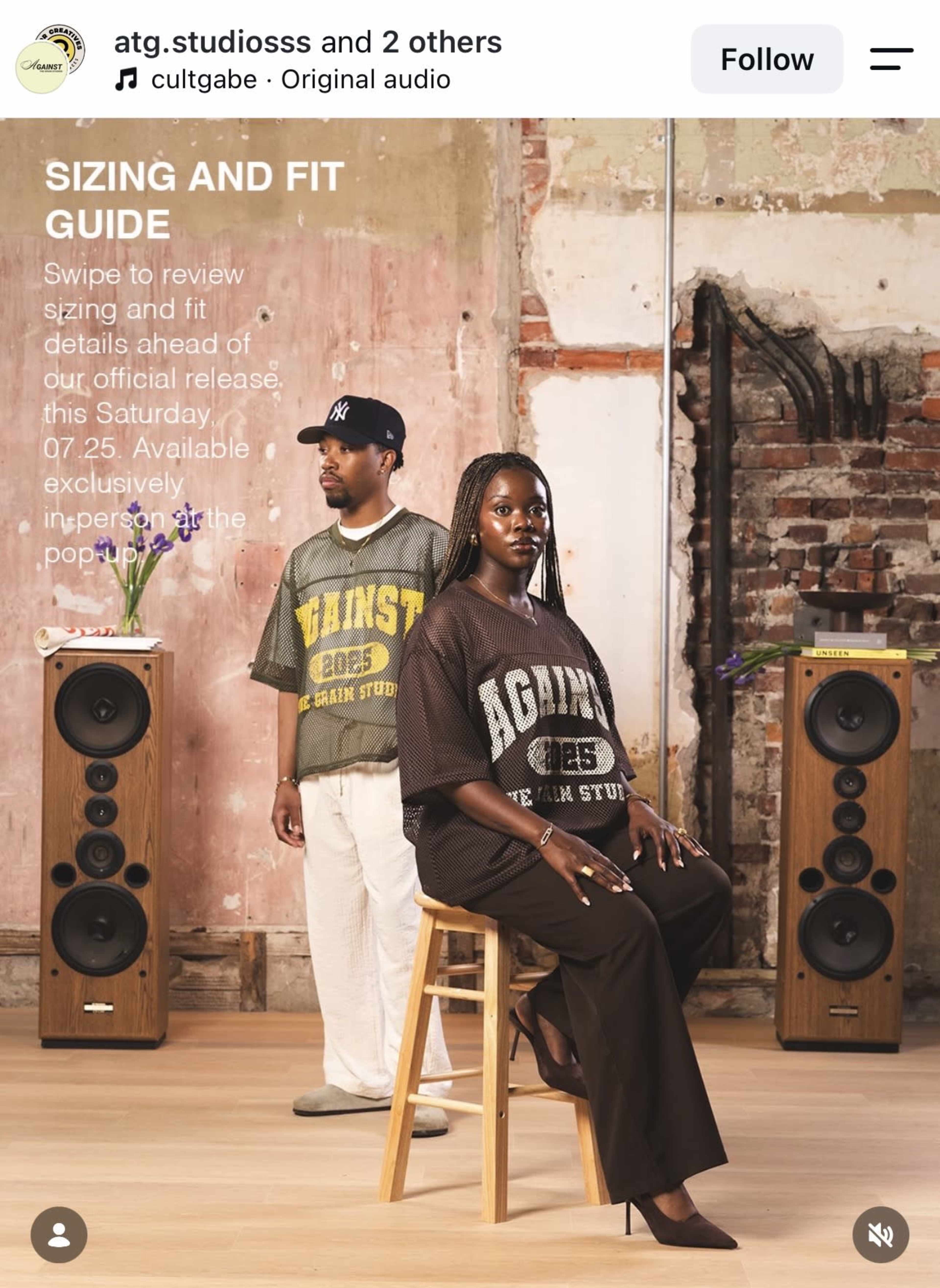 A man and a woman pose in a studio setting with large speakers, showcasing oversized clothing while a sizing and fit guide is displayed.