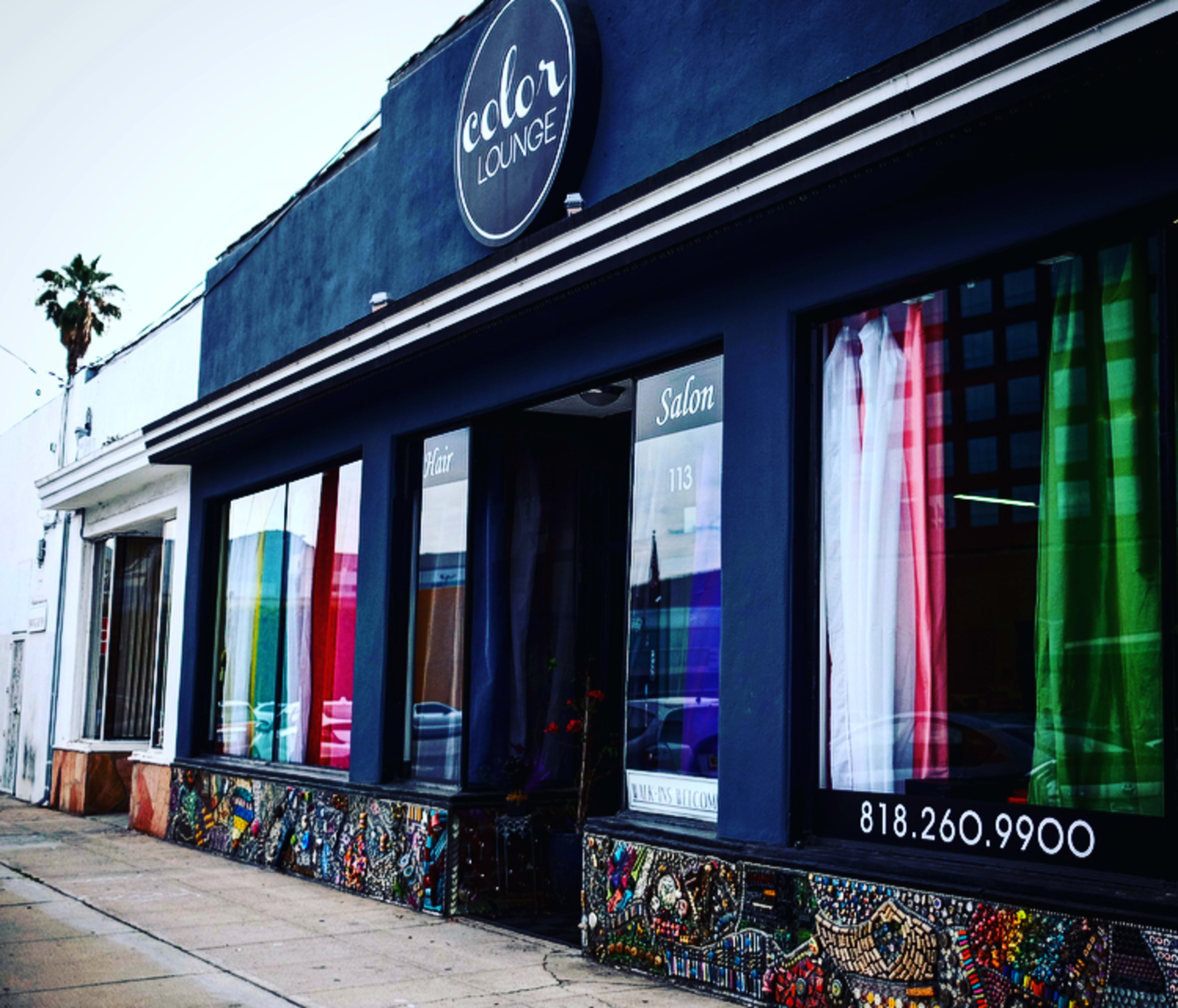 The image shows a salon called "Color Lounge," featuring colorful curtains in the windows and decorative mosaic tiles on the lower part of the exterior wall.