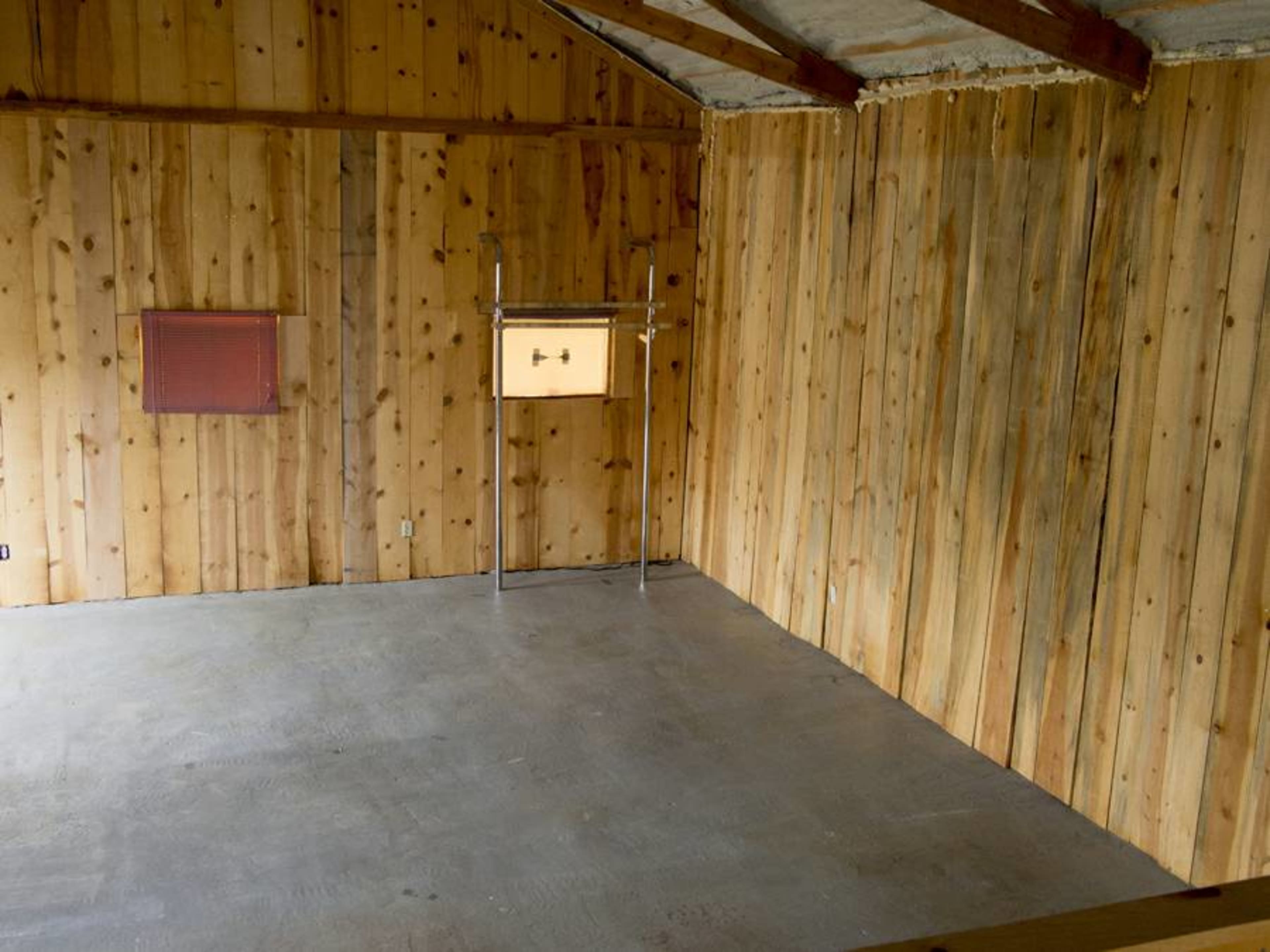 The room features wooden walls, a concrete floor, and a metal frame with a box positioned in the center.