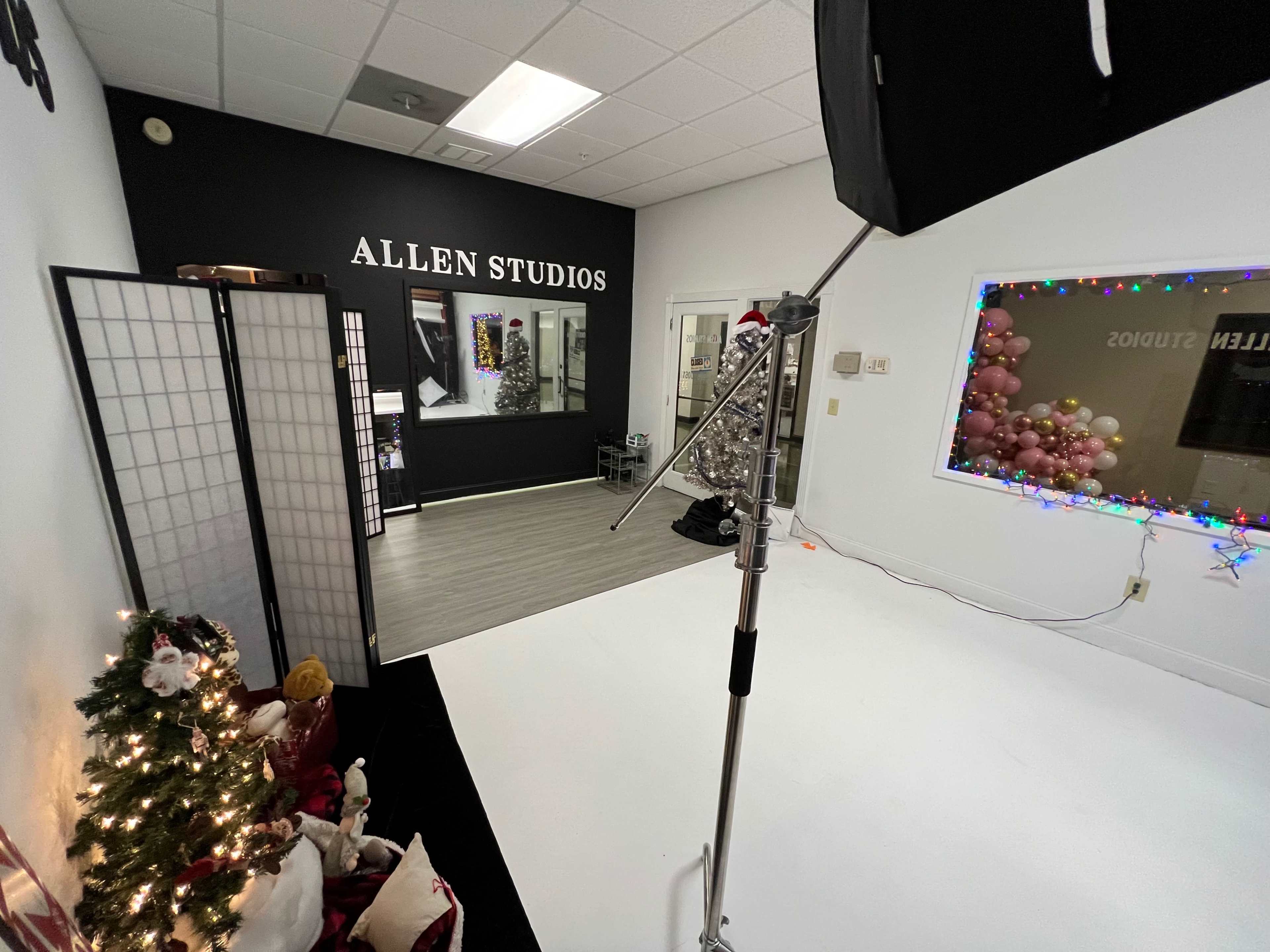 A photography studio with a black wall labeled "ALLEN STUDIOS," a decorated Christmas tree, and colorful lights along a window.